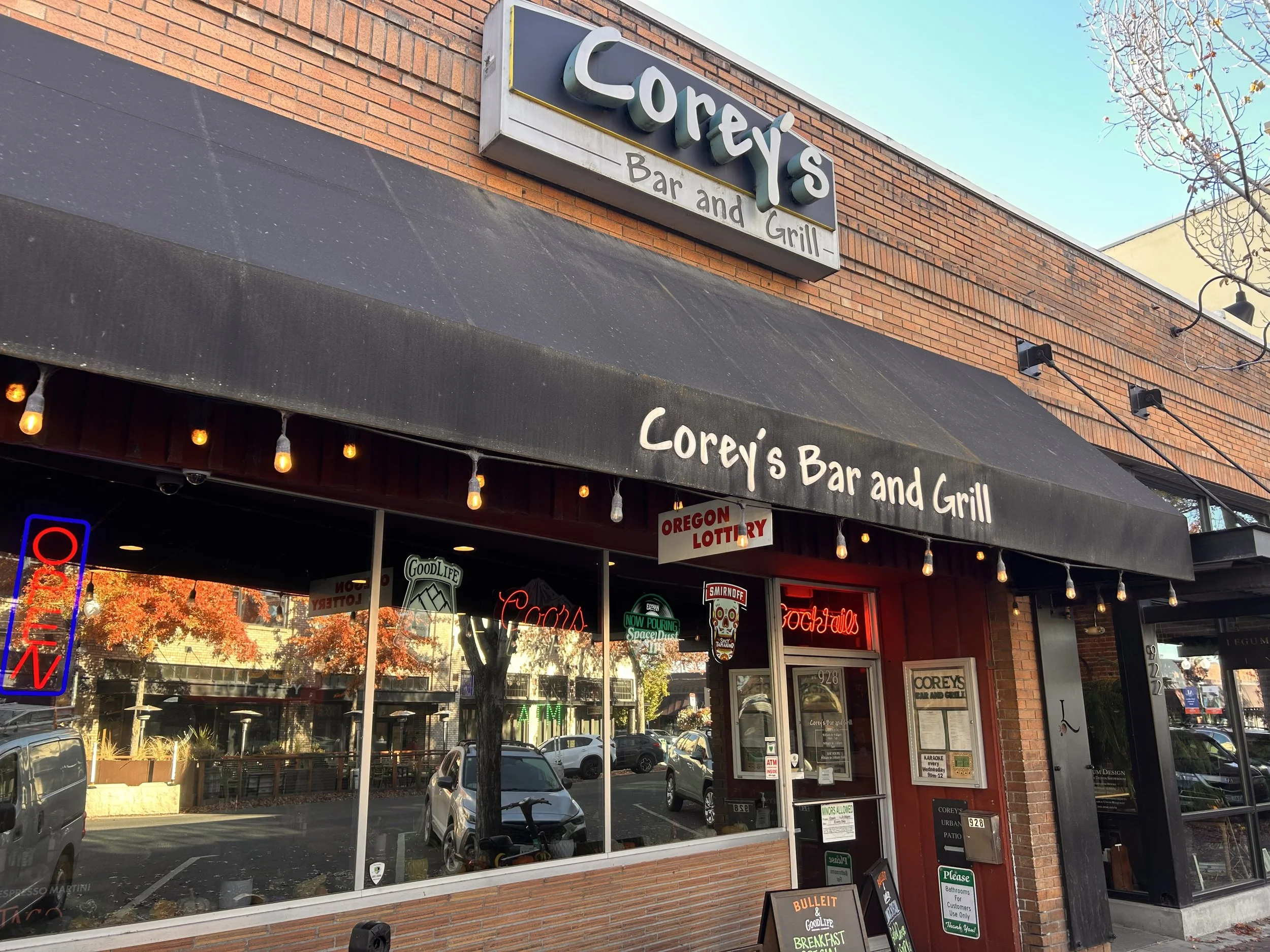 Exterior view of Corey’s Bar and Grill with a brick building, large glass windows, a black awning, and illuminated signage.