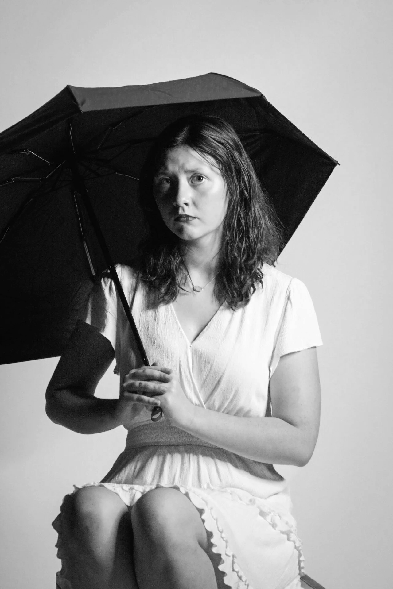 Black-and-white portrait of a woman in a white dress holding an open black umbrella.