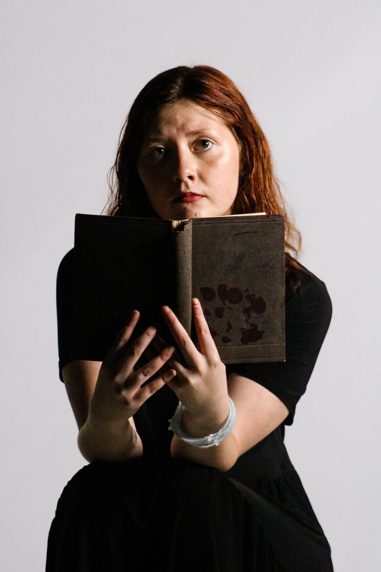 Woman in black clothing holding an open vintage book against a plain background