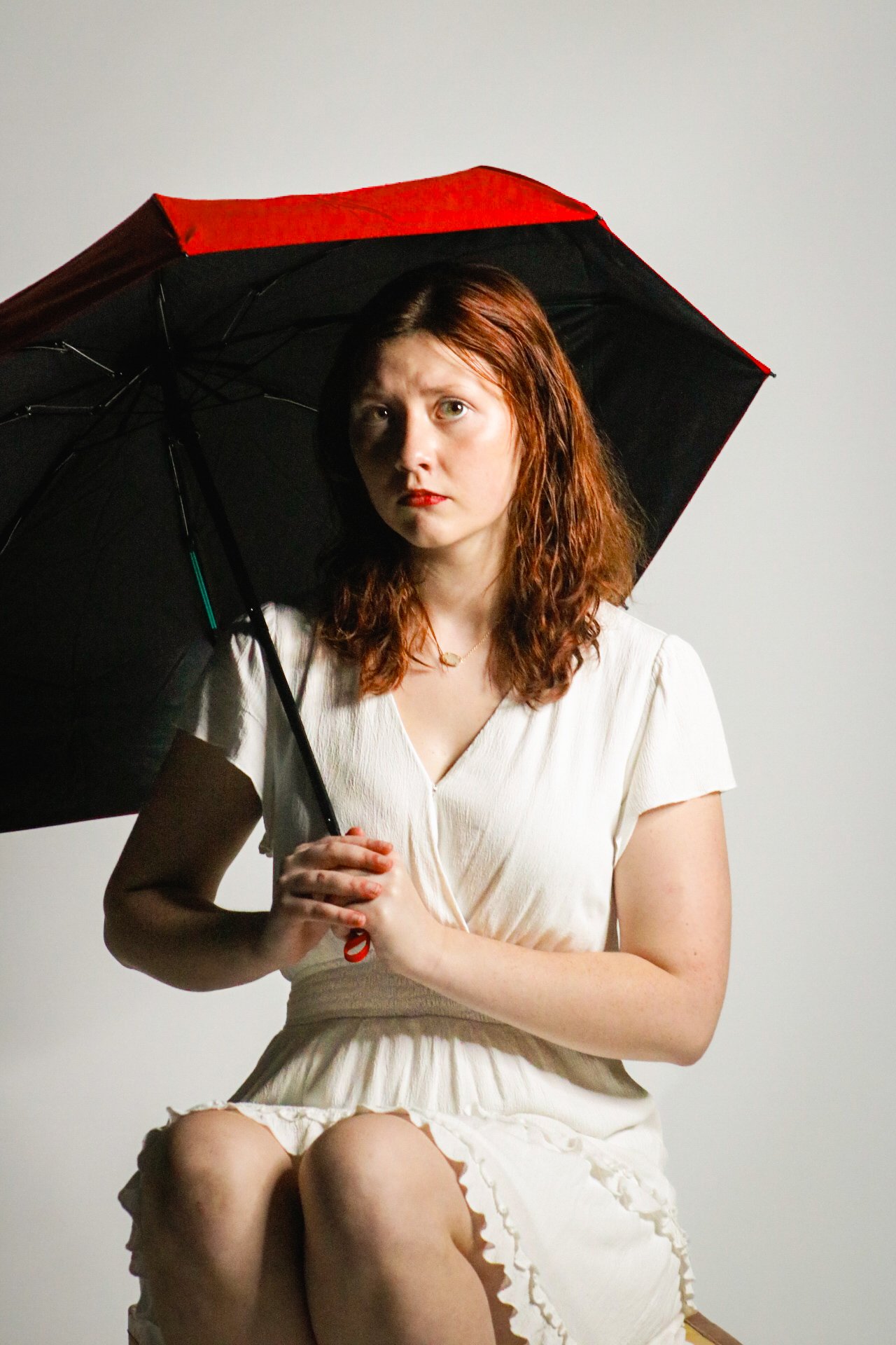 Woman in a white dress holding a black-and-red umbrella