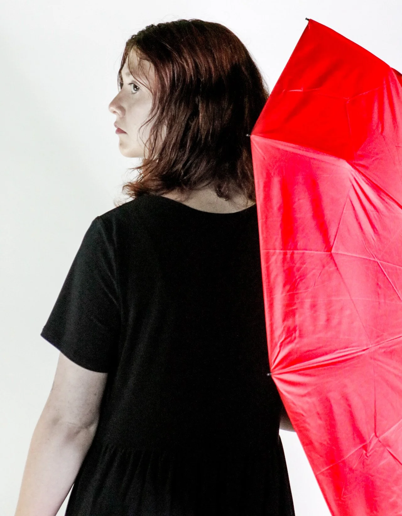 Woman in a black dress standing beside a large red umbrella against a white background