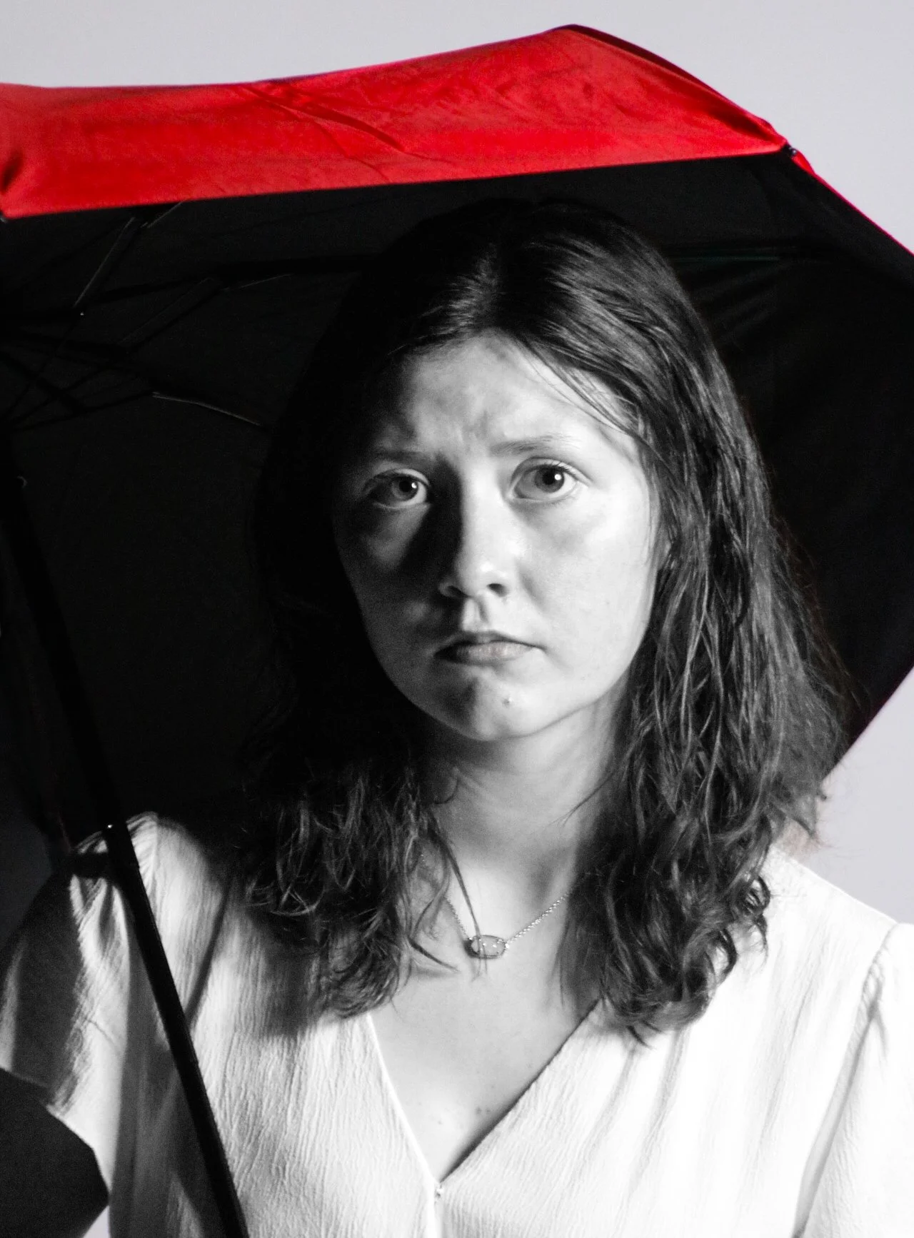 Black-and-white portrait of a woman holding an open umbrella with a red canopy.