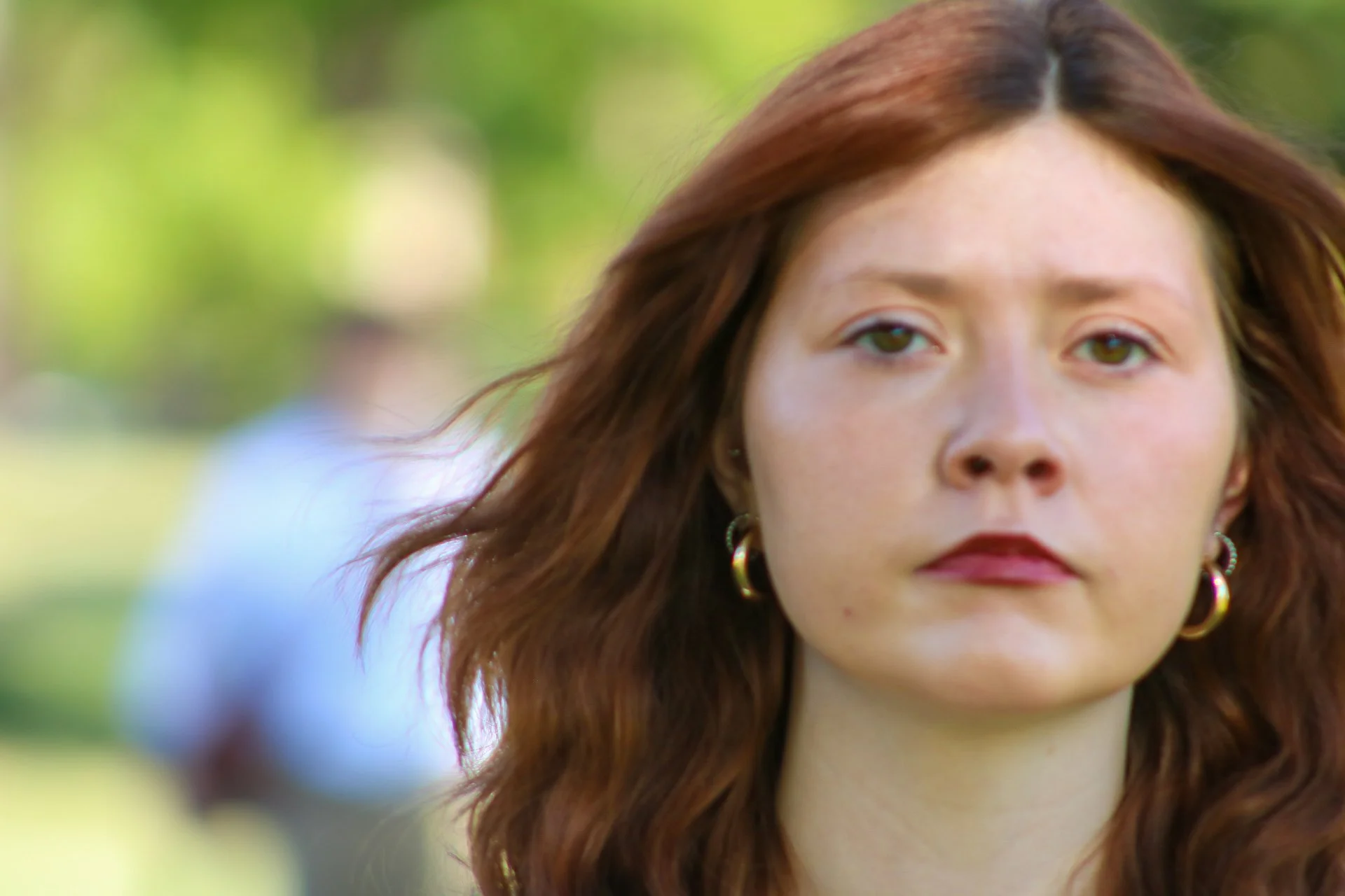 Close-up portrait of a woman with long brown hair and hoop earrings outdoors