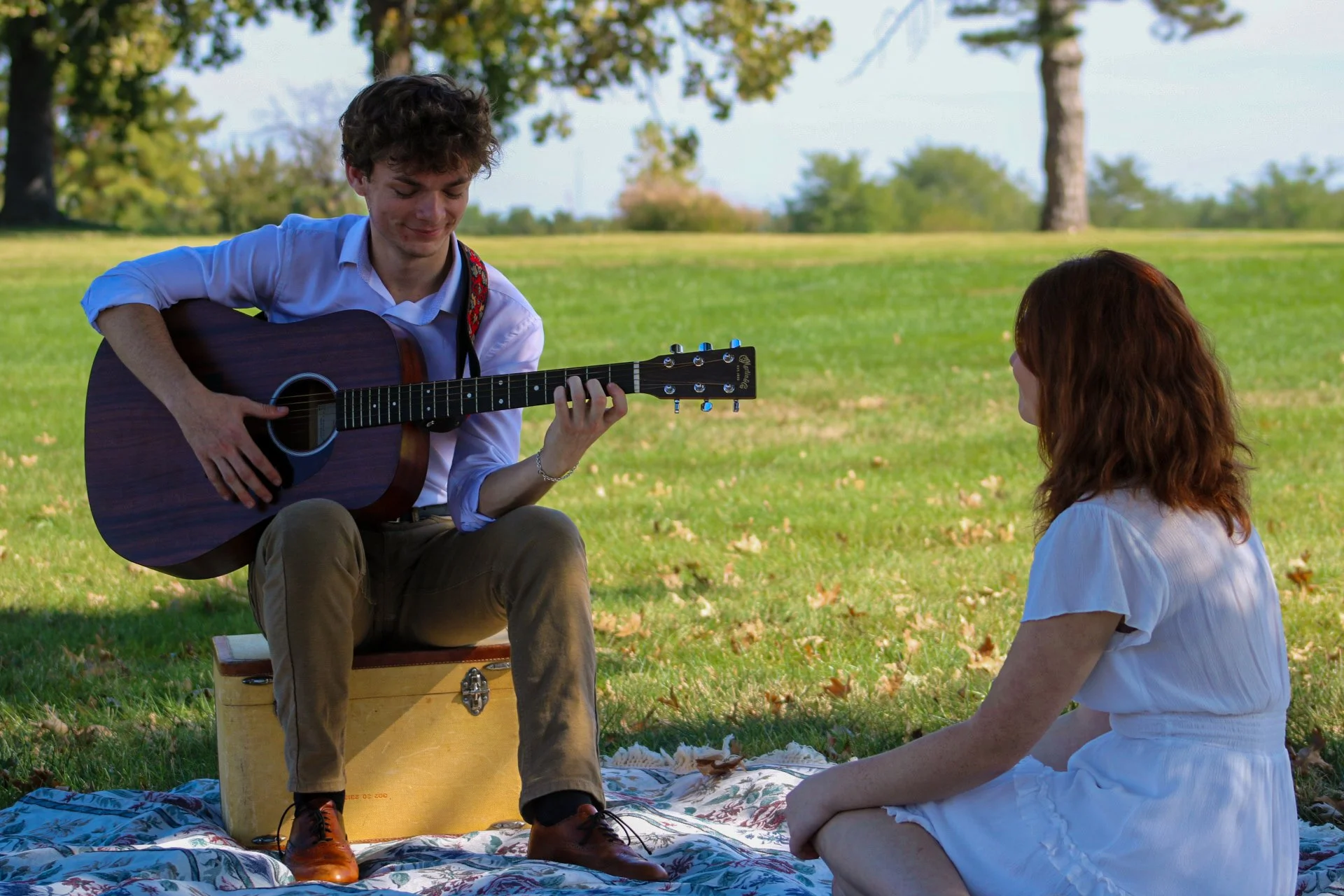 Young man playing acoustic guitar to a woman during a picnic in a sunny park