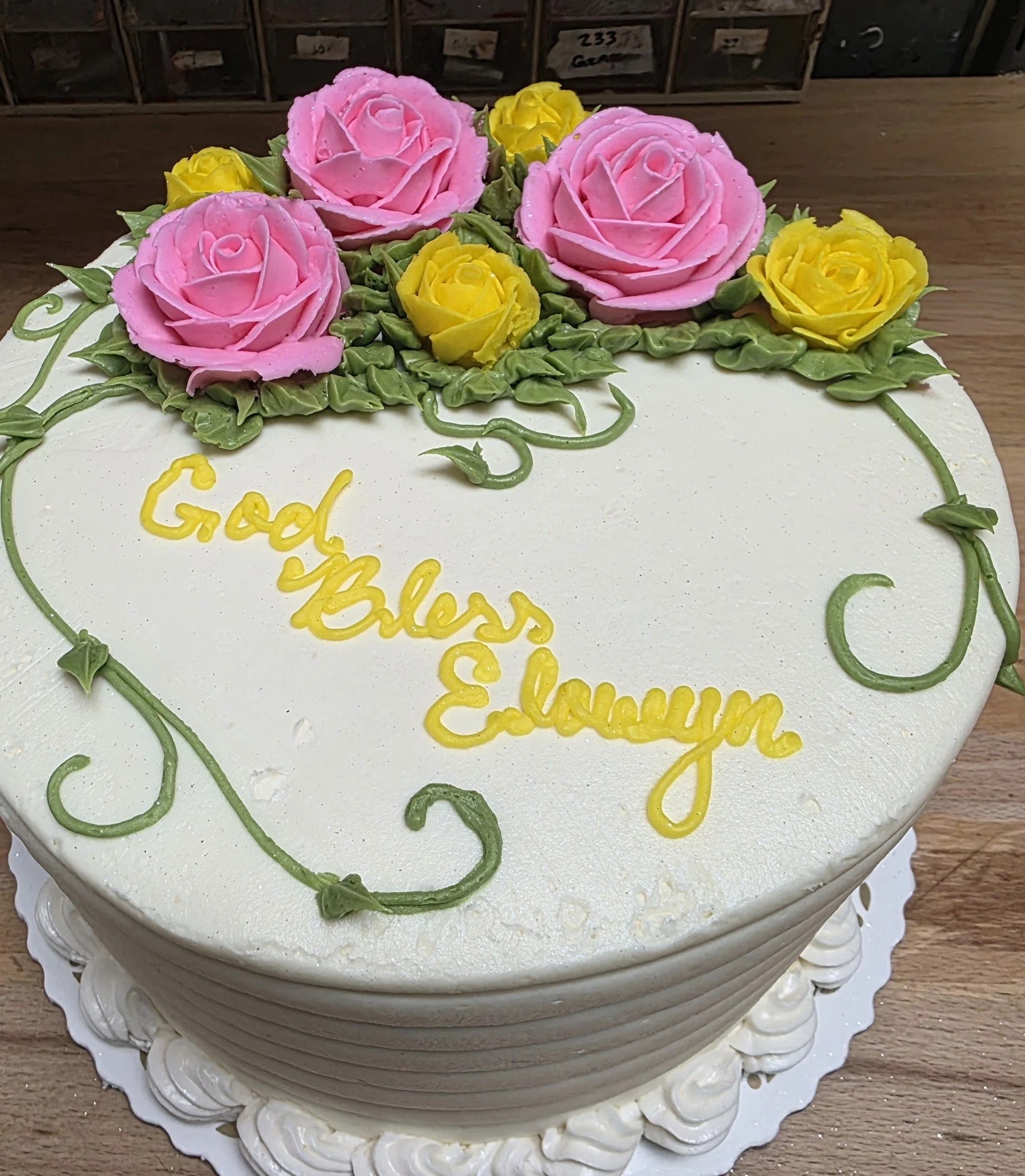 Pink and yellow roses with trailing green leaves on a round cake made by Jess.