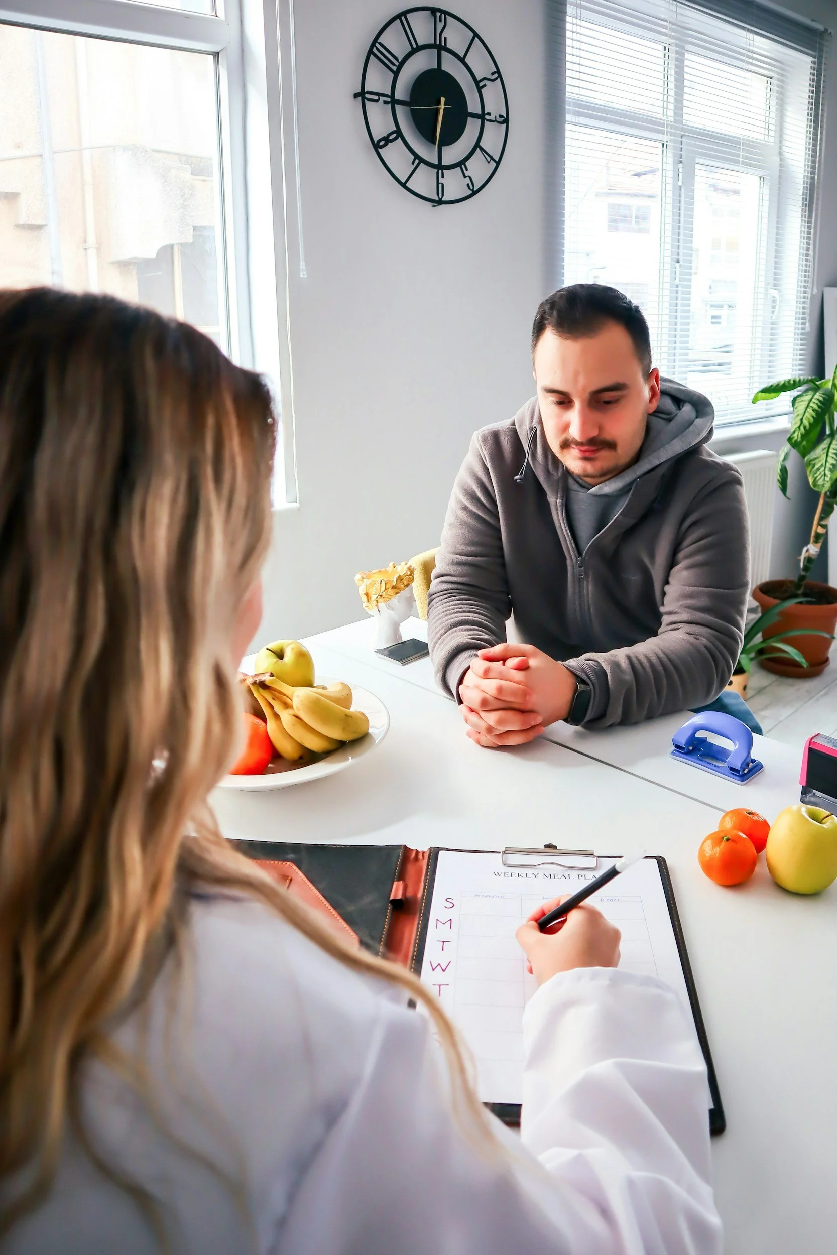 Consultation nutritionnelle à domicile : une nutritionniste planifie les repas avec un homme à table, entourés de fruits.