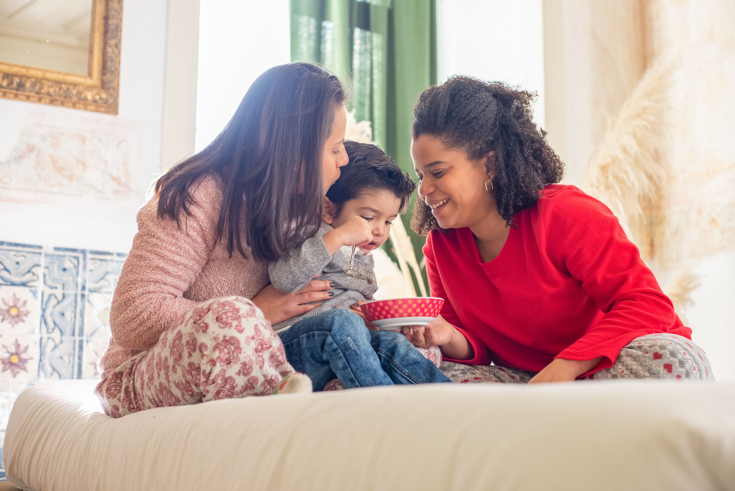 Deux femmes nourrissent un jeune enfant à la cuillère dans un intérieur chaleureux.