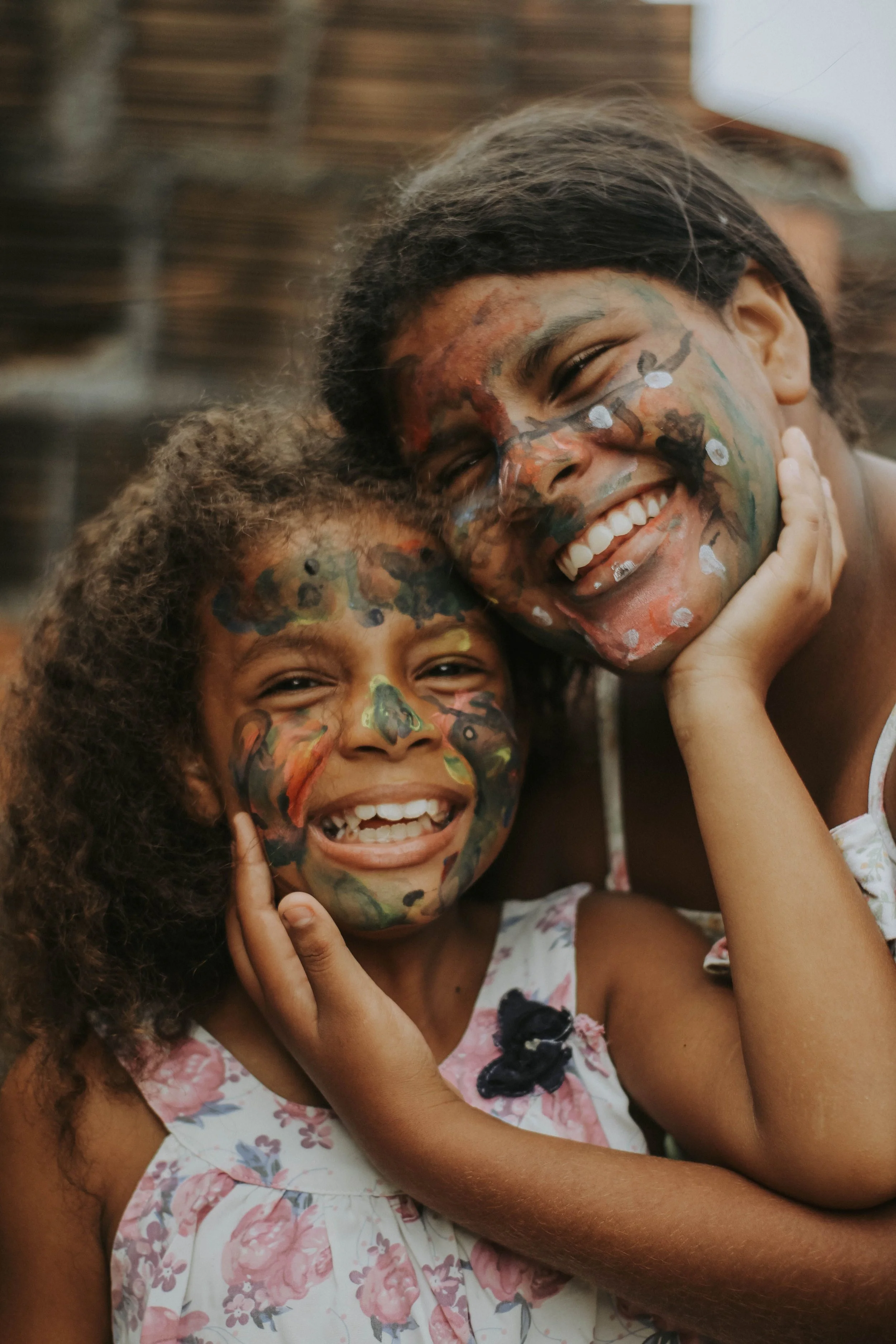 Deux personnes souriantes, le visage peint de motifs colorés et de papillons, posent ensemble pour un selfie.