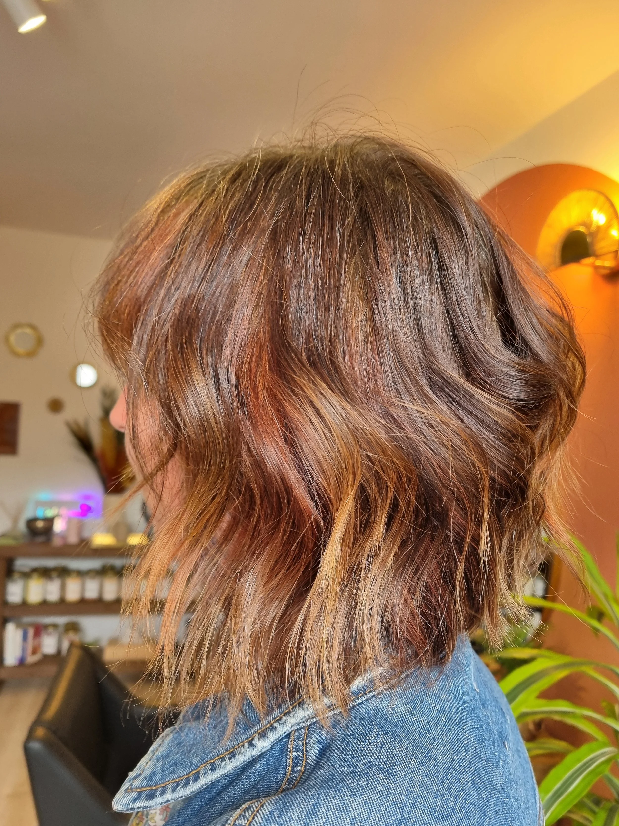 Cheveux courts, ondulés, de couleur châtain clair avec des reflets auburn, portant un jean.