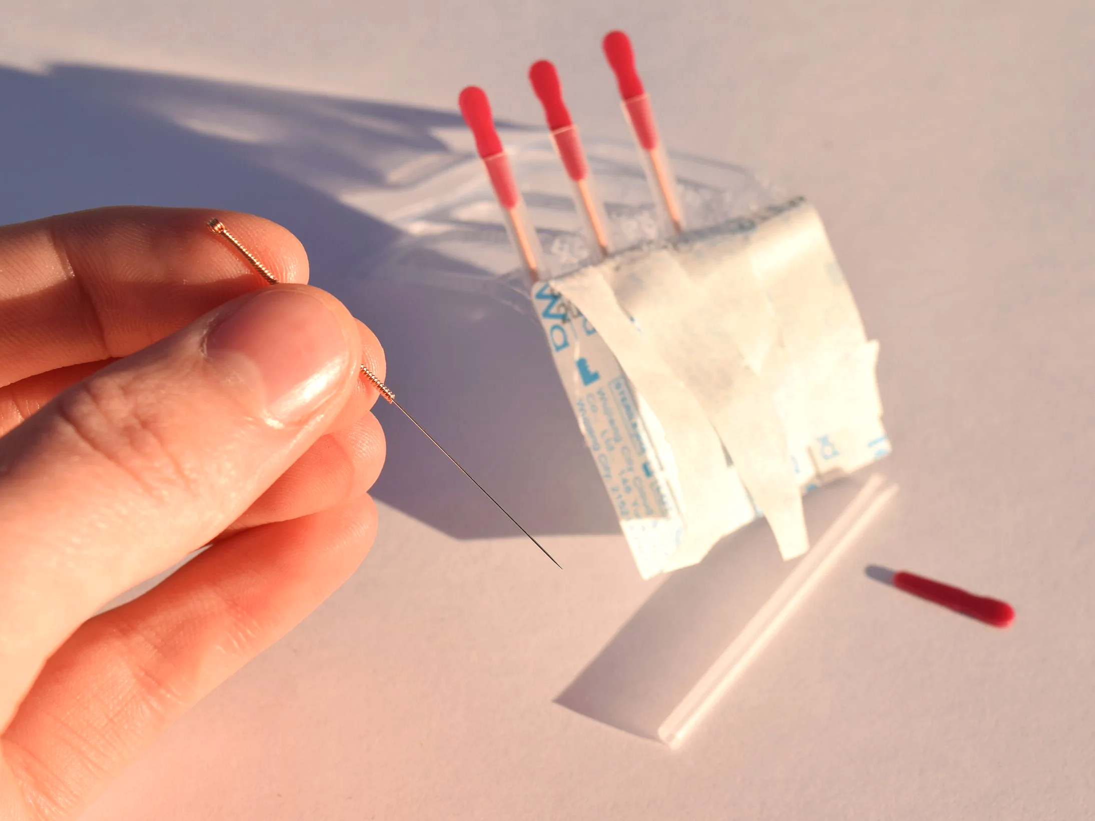 A person's hand holding a small acupuncture needle, with three more acupuncture needles in their packaging.