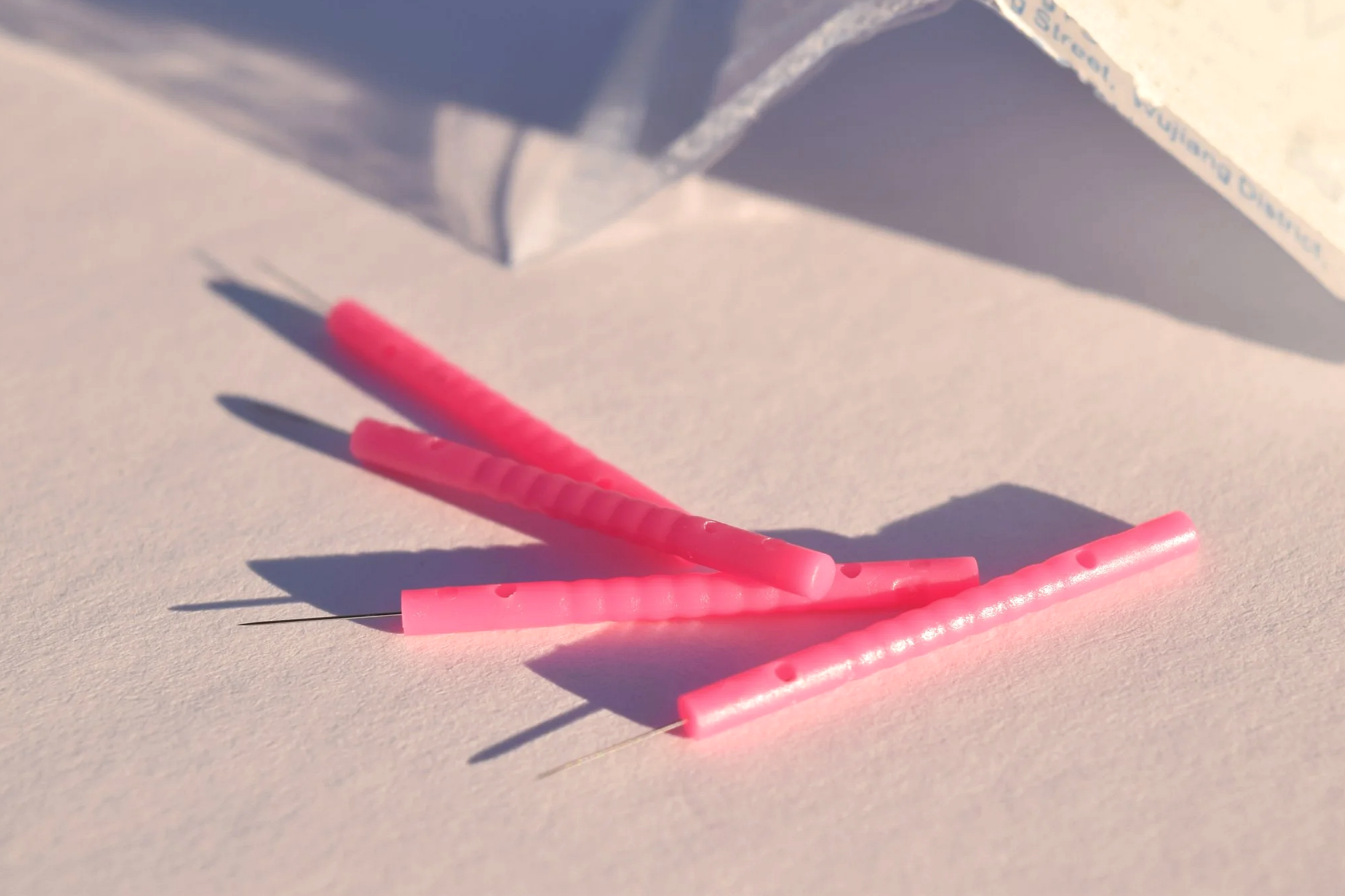 Close-up of four pink acupuncture needles on a white surface with shadows cast by sunlight.