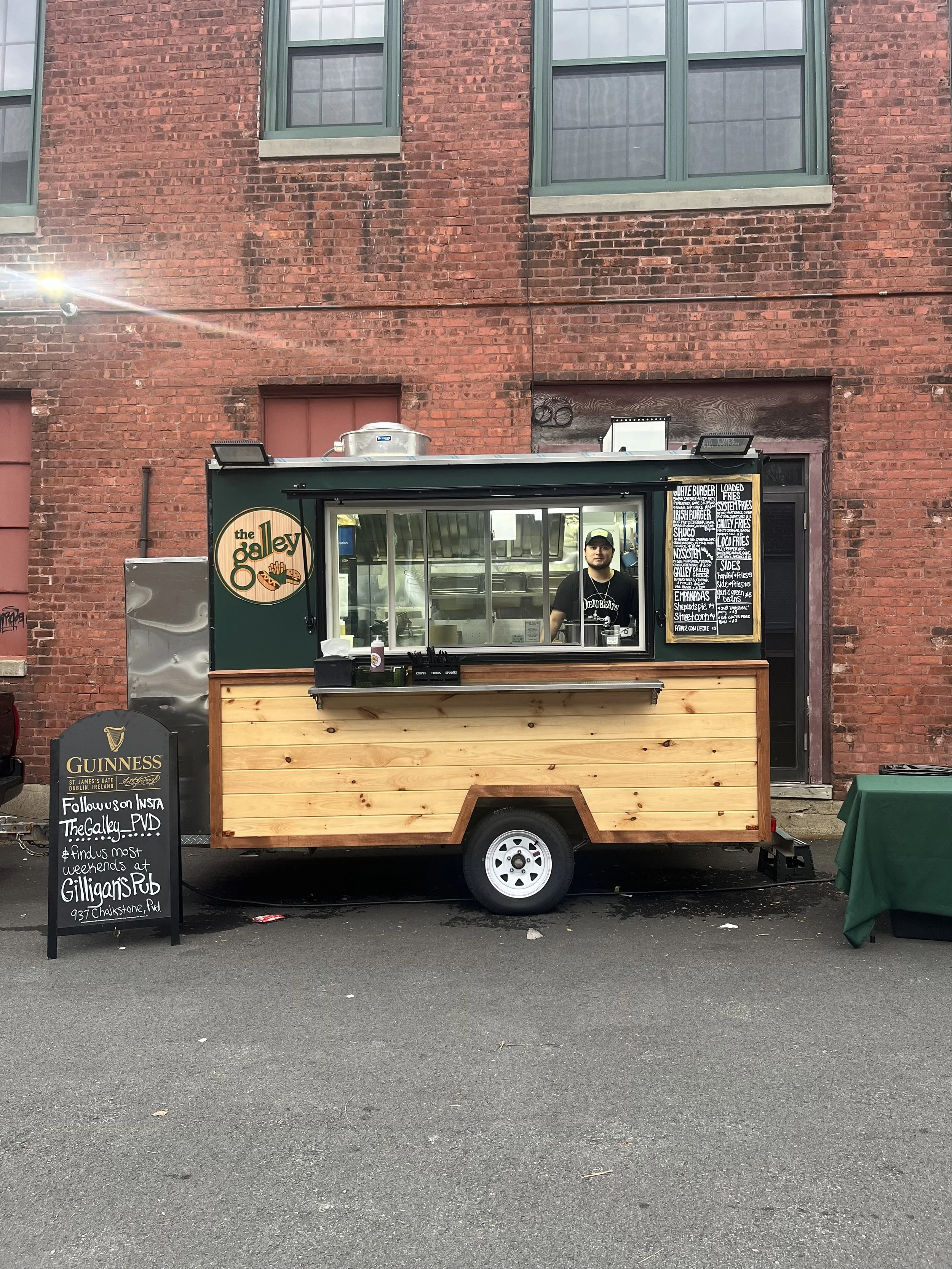 The Galley food truck serving burgers and fries outside a brick building, with a vendor at the service window and menu boards displayed.