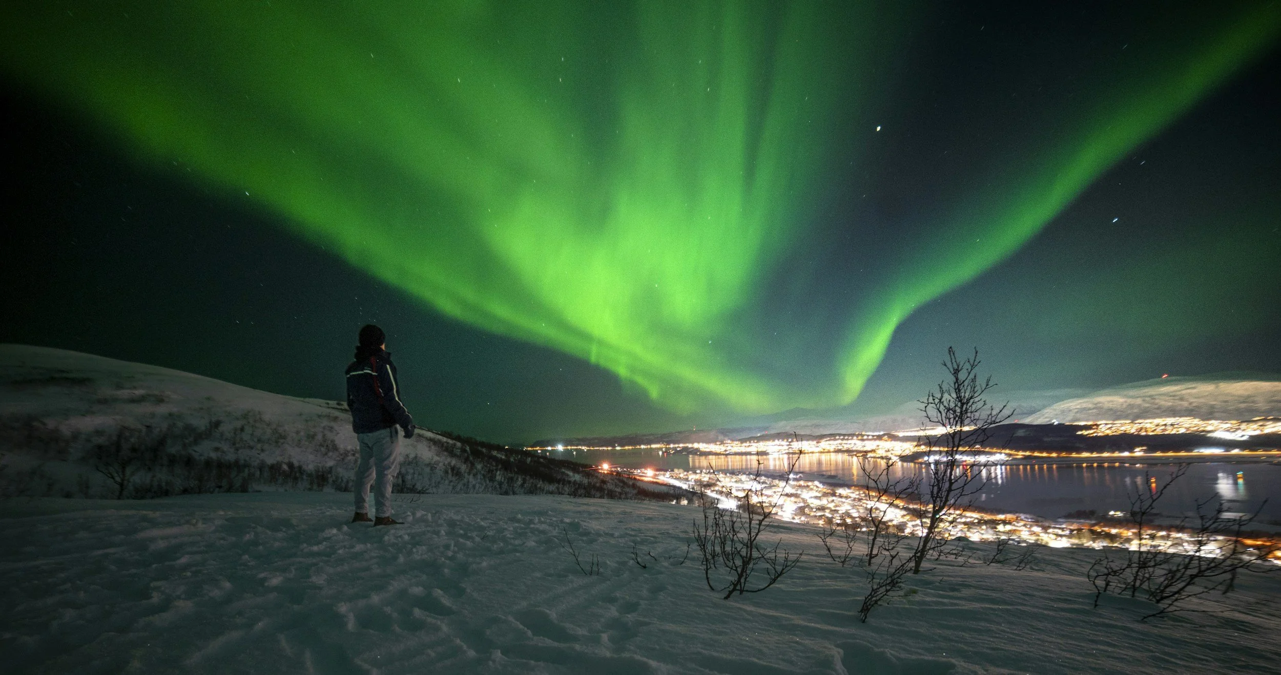 Persona che osserva le luci dell'aurora boreale nel cielo notturno sopra un paesaggio innevato.