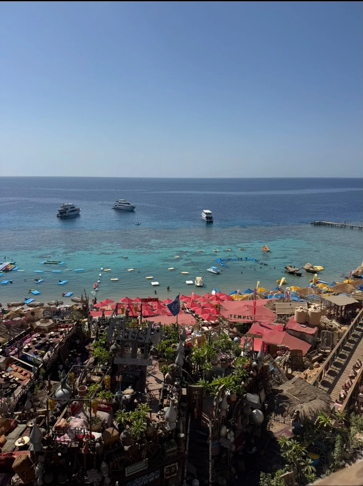 Spiaggia con ombrelloni colorati, barche a vela e yacht in mare, mare blu e cielo azzurro