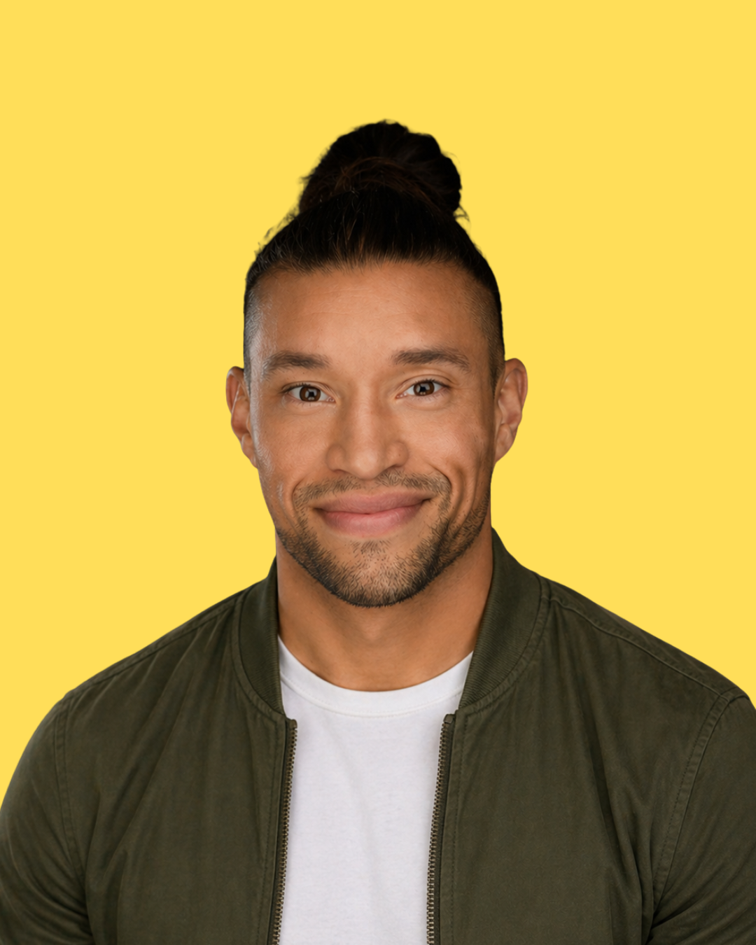 Smiling man with a topknot and trimmed beard wearing a green jacket over a white shirt against a yellow background