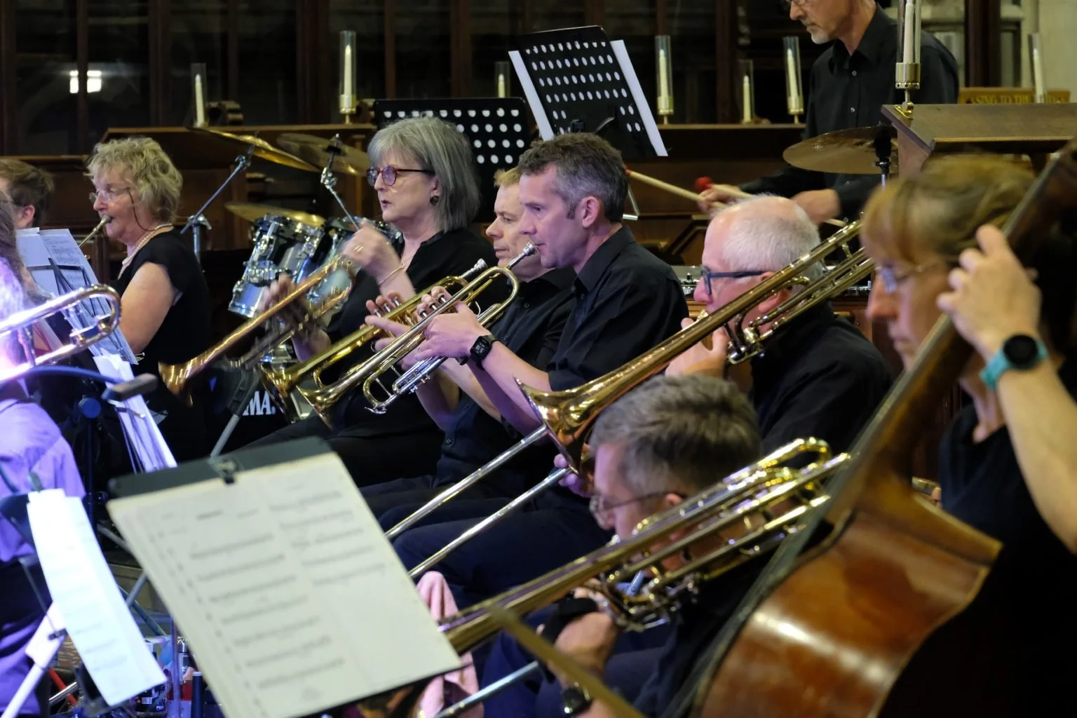 An orchestra performing, with musicians playing brass and percussion instruments, seated in a concert hall.