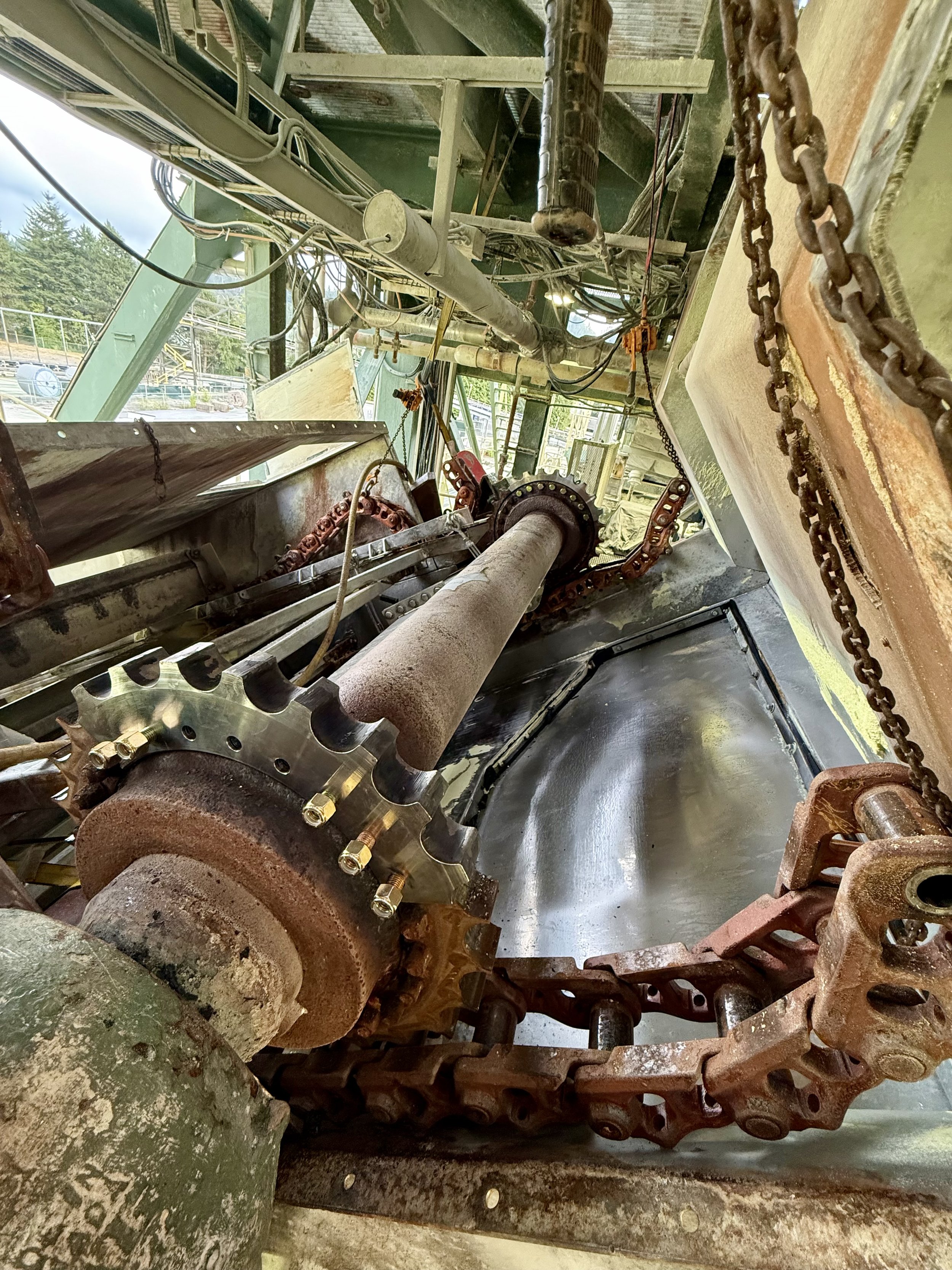 Close-up view of mechanical parts, including rusted gears, chains, and metal rods, in an industrial or construction setting.