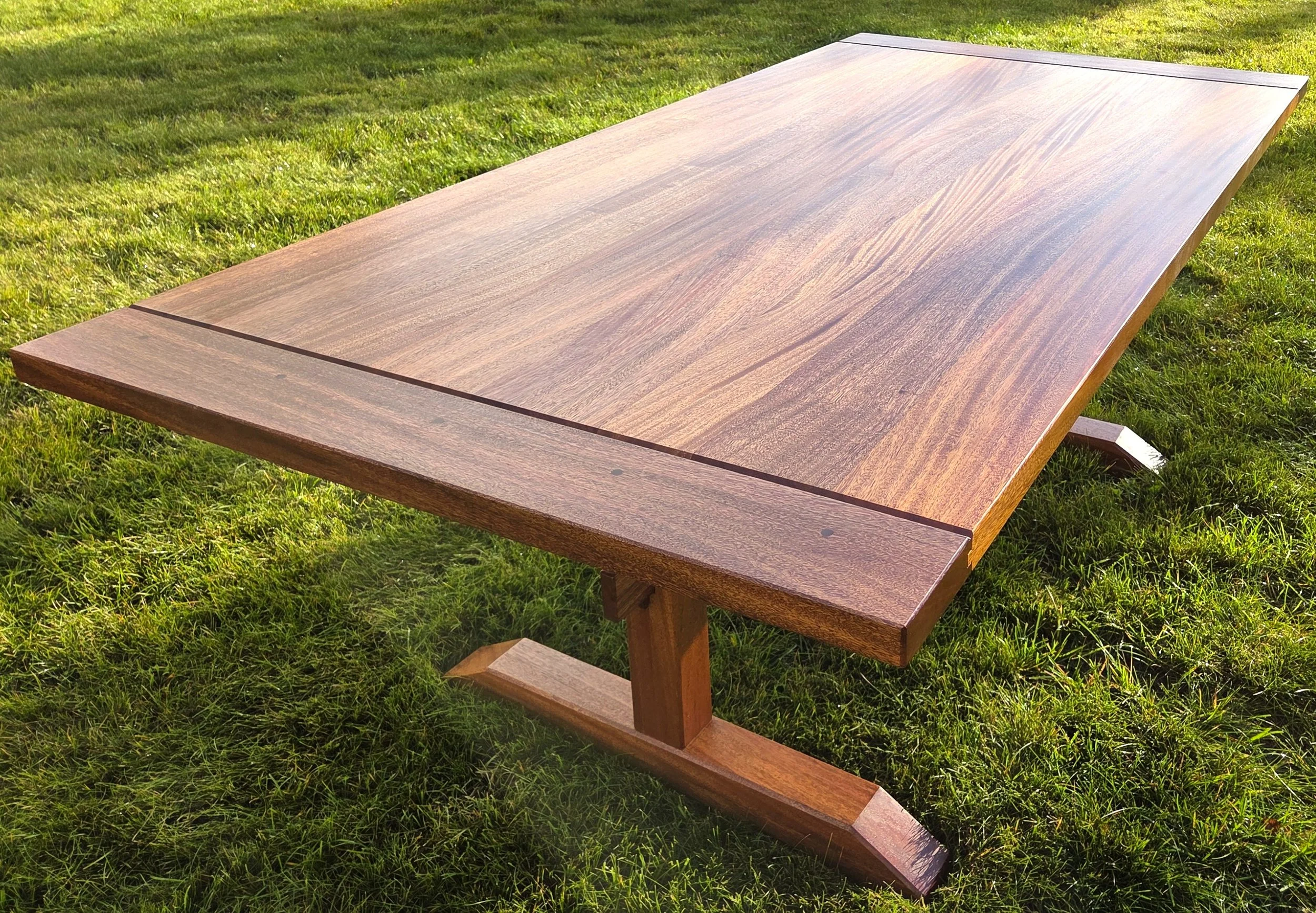 Large wooden outdoor picnic table with attached benches on a sunny grassy lawn