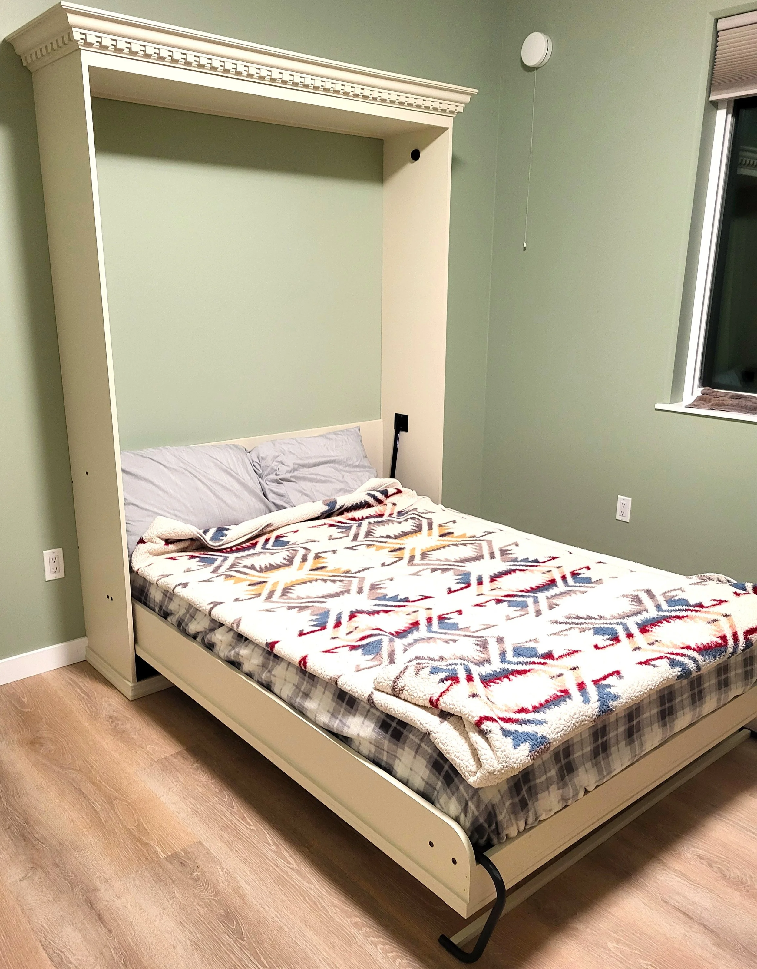 Bedroom with a white built-in bed, patterned blanket, green walls, decorative molding, and window blinds
