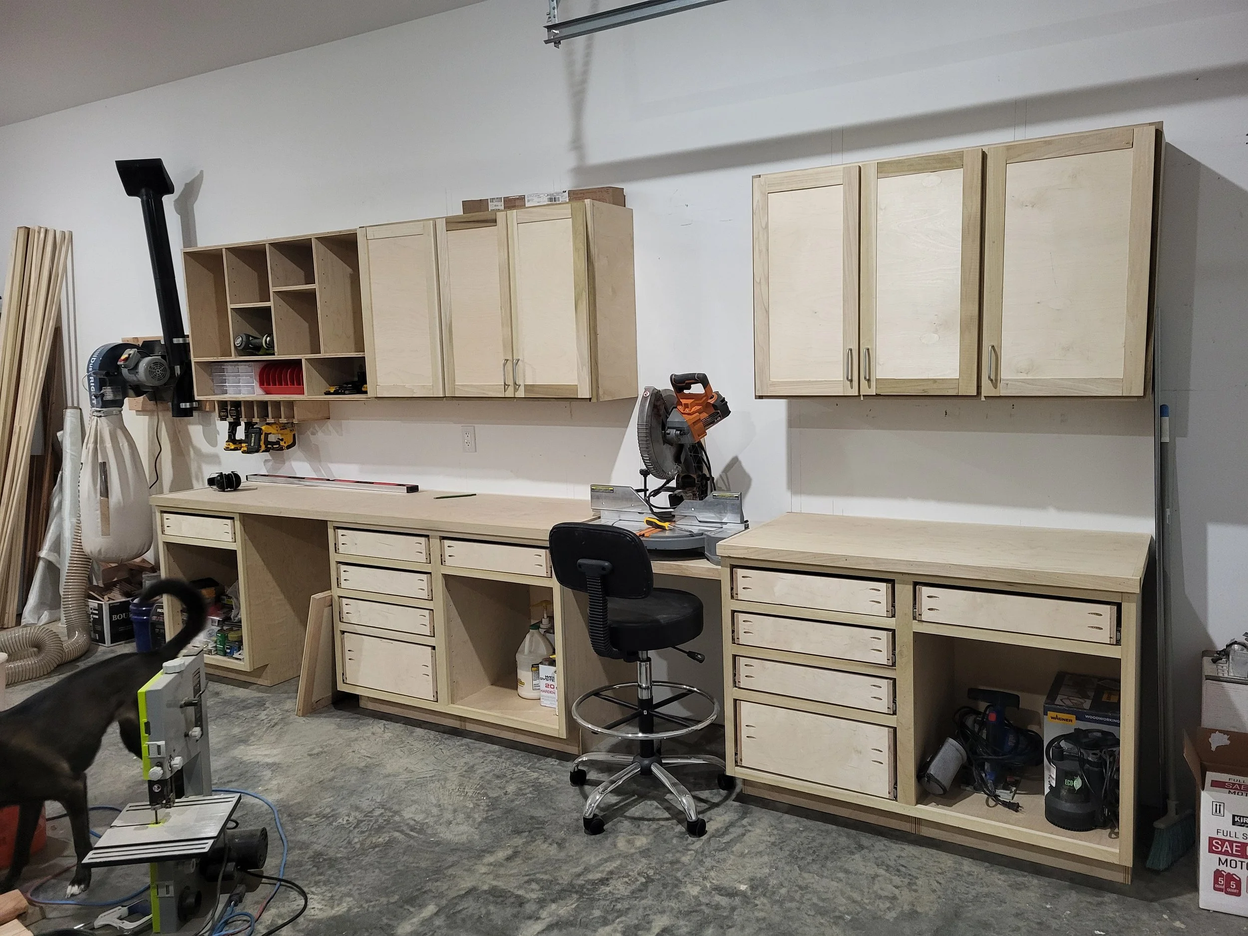 Custom plywood woodworking workshop with built-in cabinets, drawers, workbenches, tools, dust collector, and miter saw