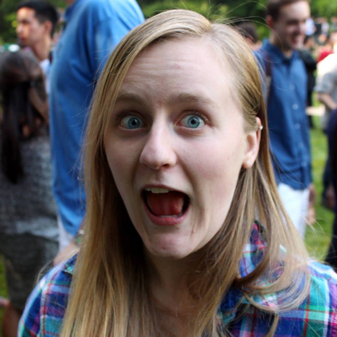 A young woman with red hair and blue eyes with an expression of surprise or shock in a crowd at an outdoor event.
