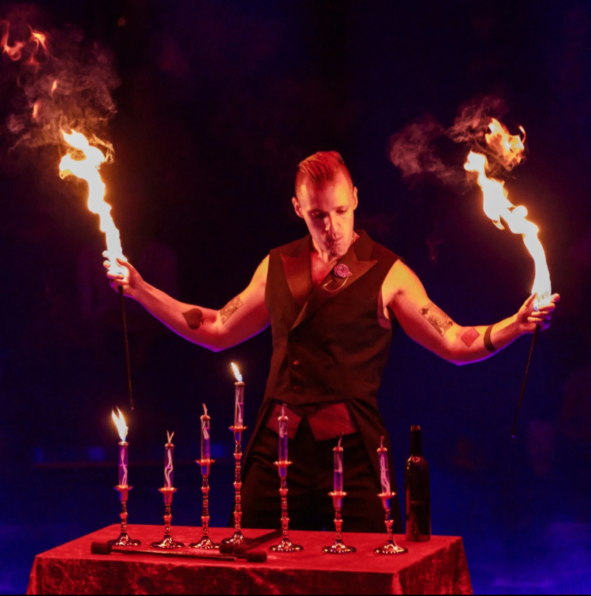 Person performing a fire eating act at a circus or performance event, with flames on torches and a spotlight background.