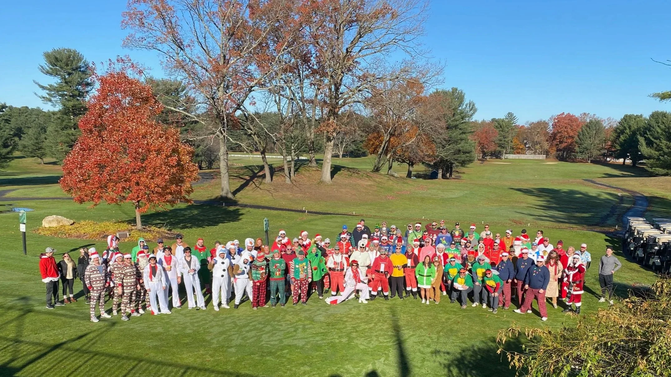 Large group in Christmas costumes posing on a golf course during autumn