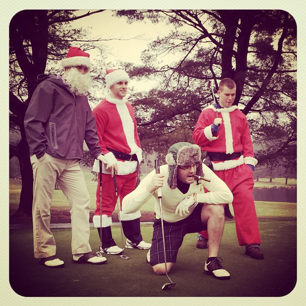 Group of four men dressed as Santa Claus and a golfer posing on a golf course