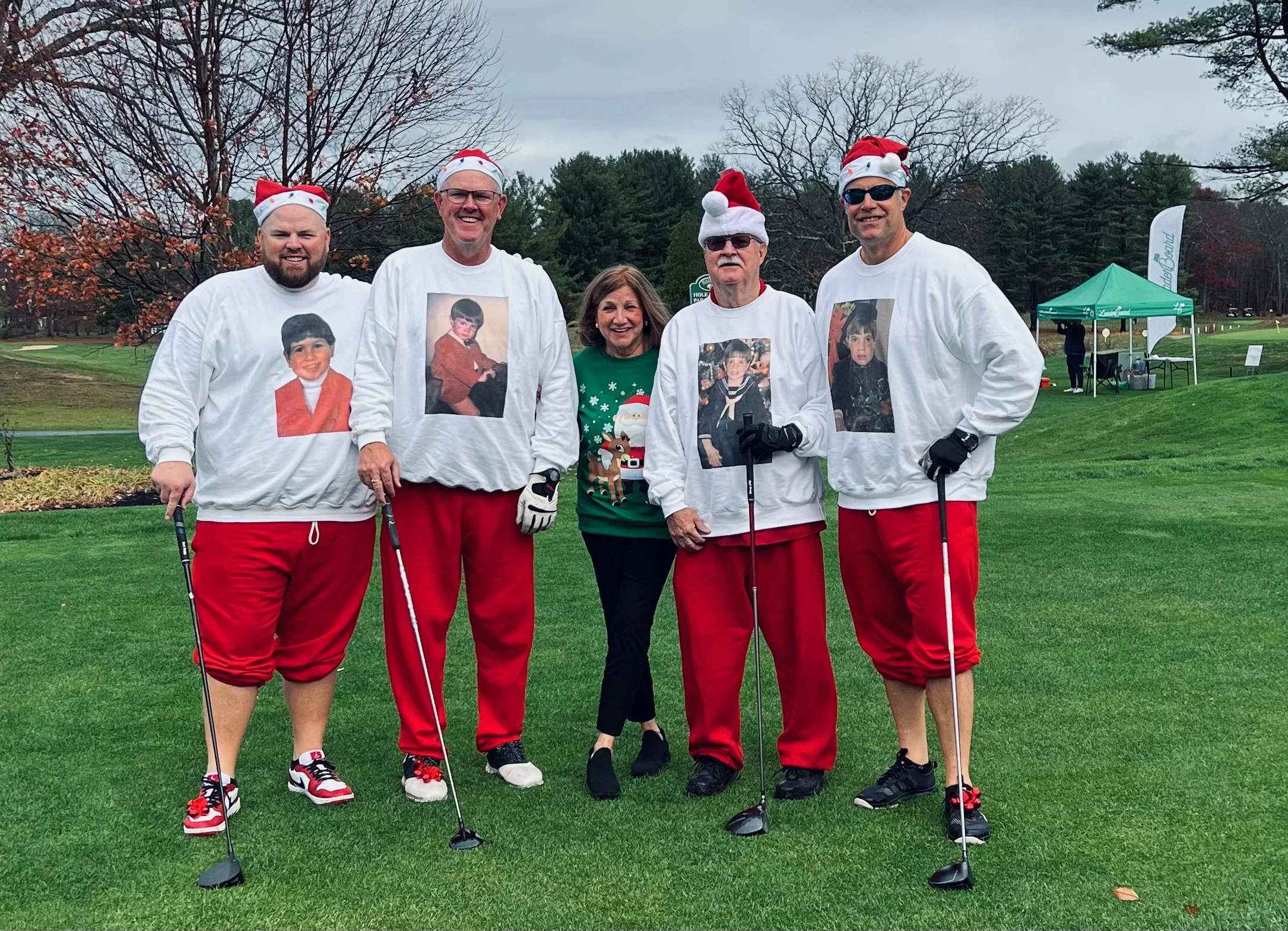 Group of golfers wearing Santa hats and Christmas-themed shirts posing with clubs on a golf course.