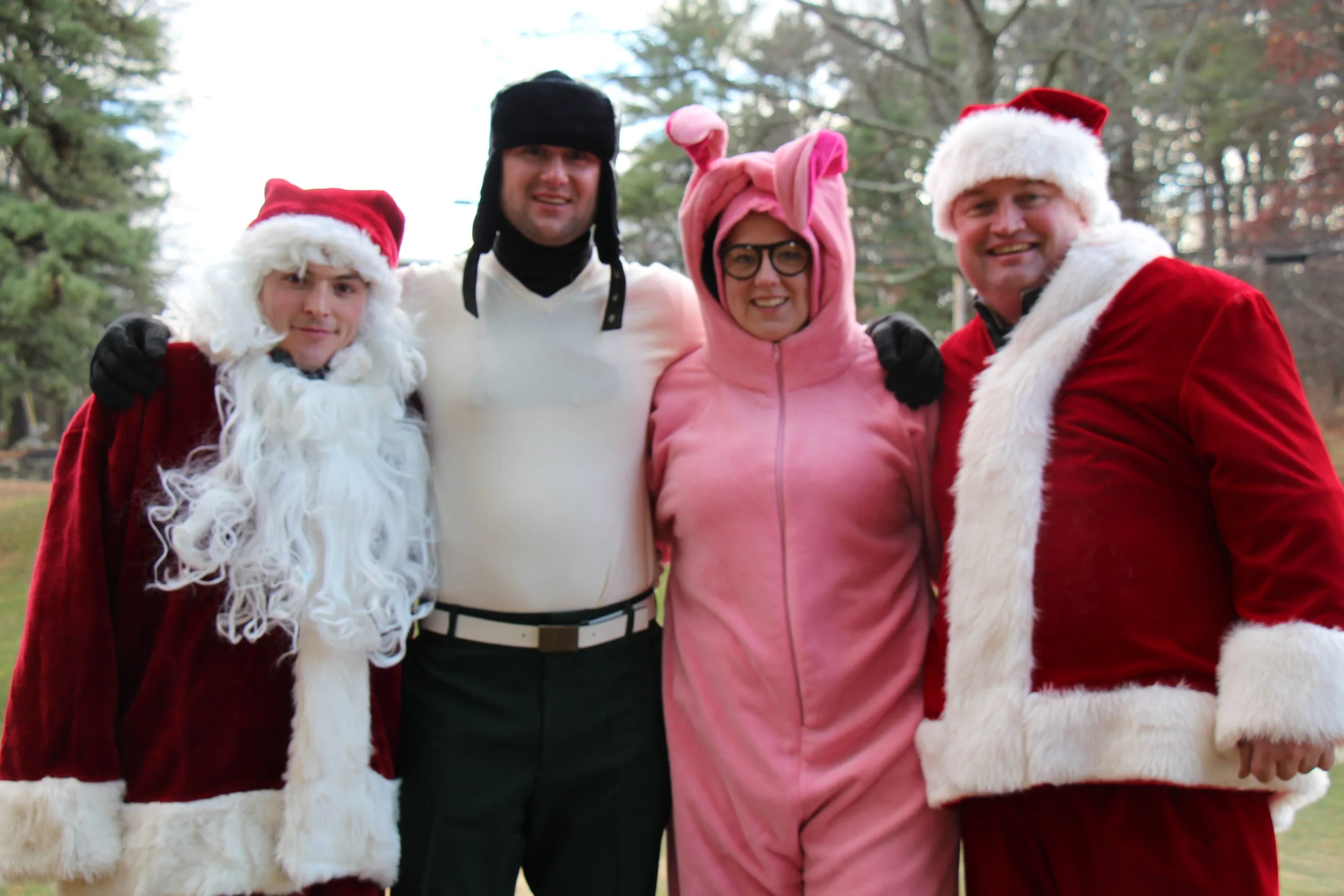 Four people posing outdoors in Santa, elf, and pink holiday costumes