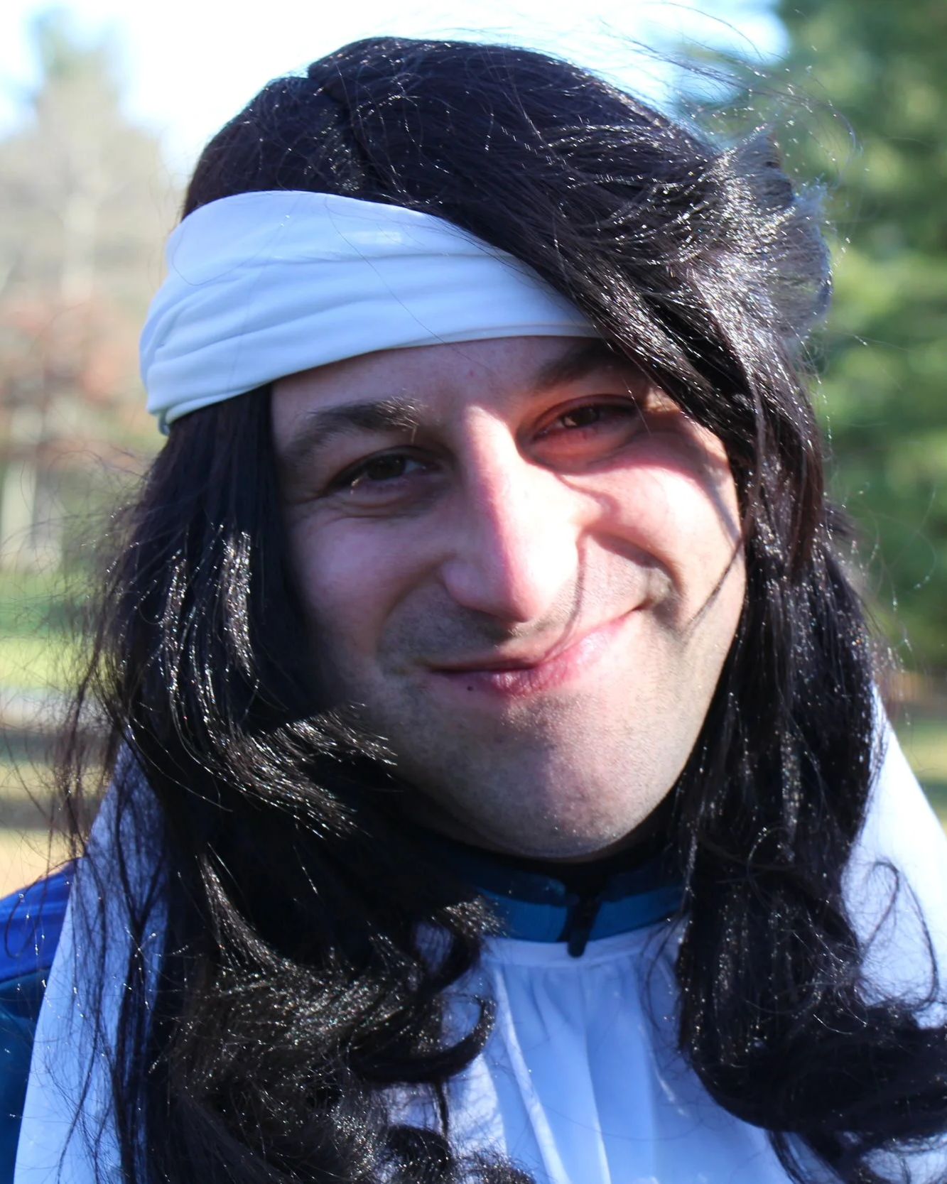 Close-up portrait of a smiling person with long dark hair and a white headband outdoors