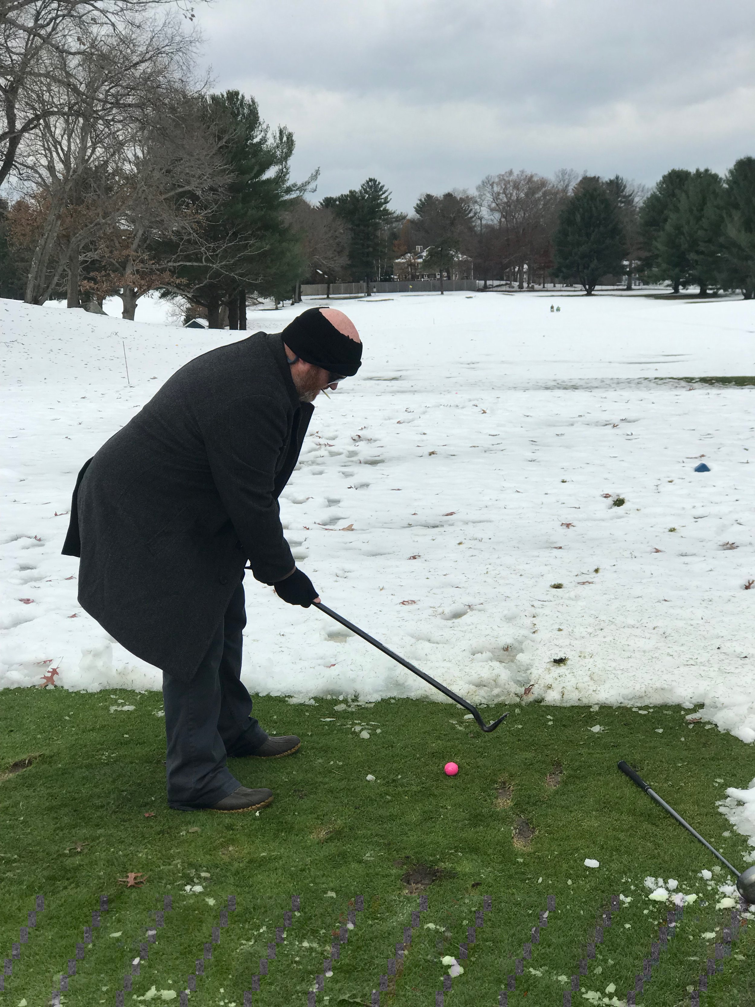 Man playing croquet on a snow-covered lawn with a mallet and pink ball