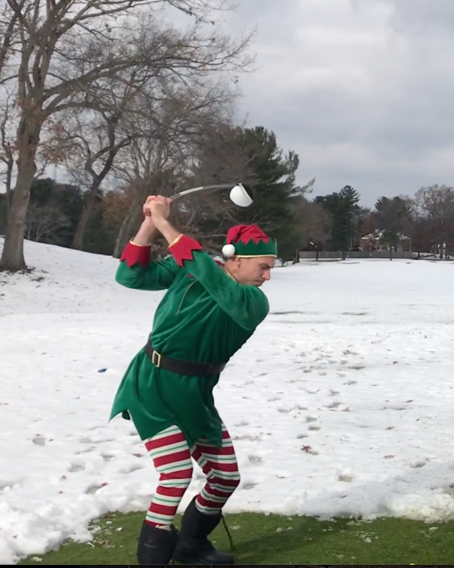 Person dressed as a Christmas elf swinging a golf club in a snowy park