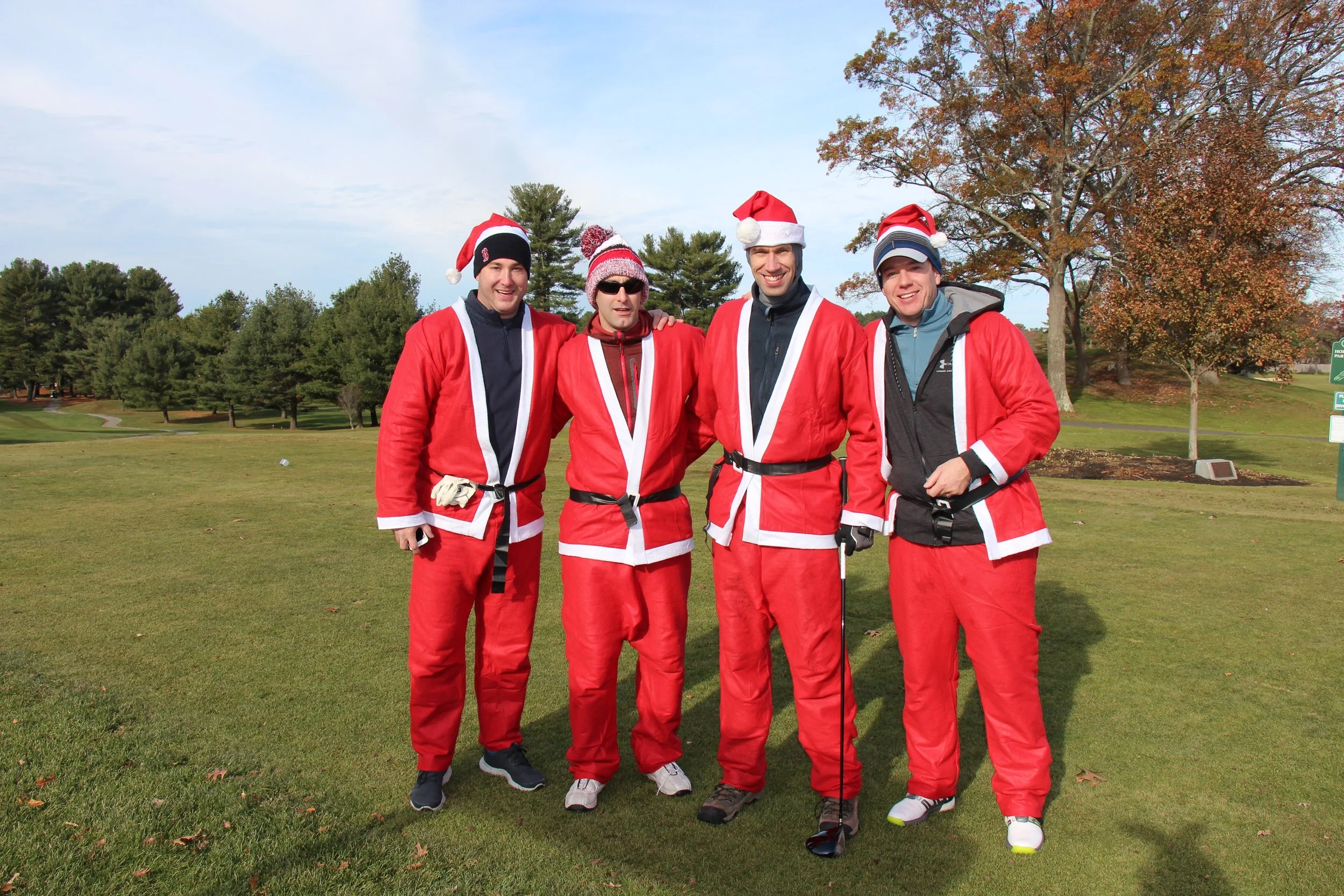 Four men in Santa Claus costumes posing on a golf course in autumn