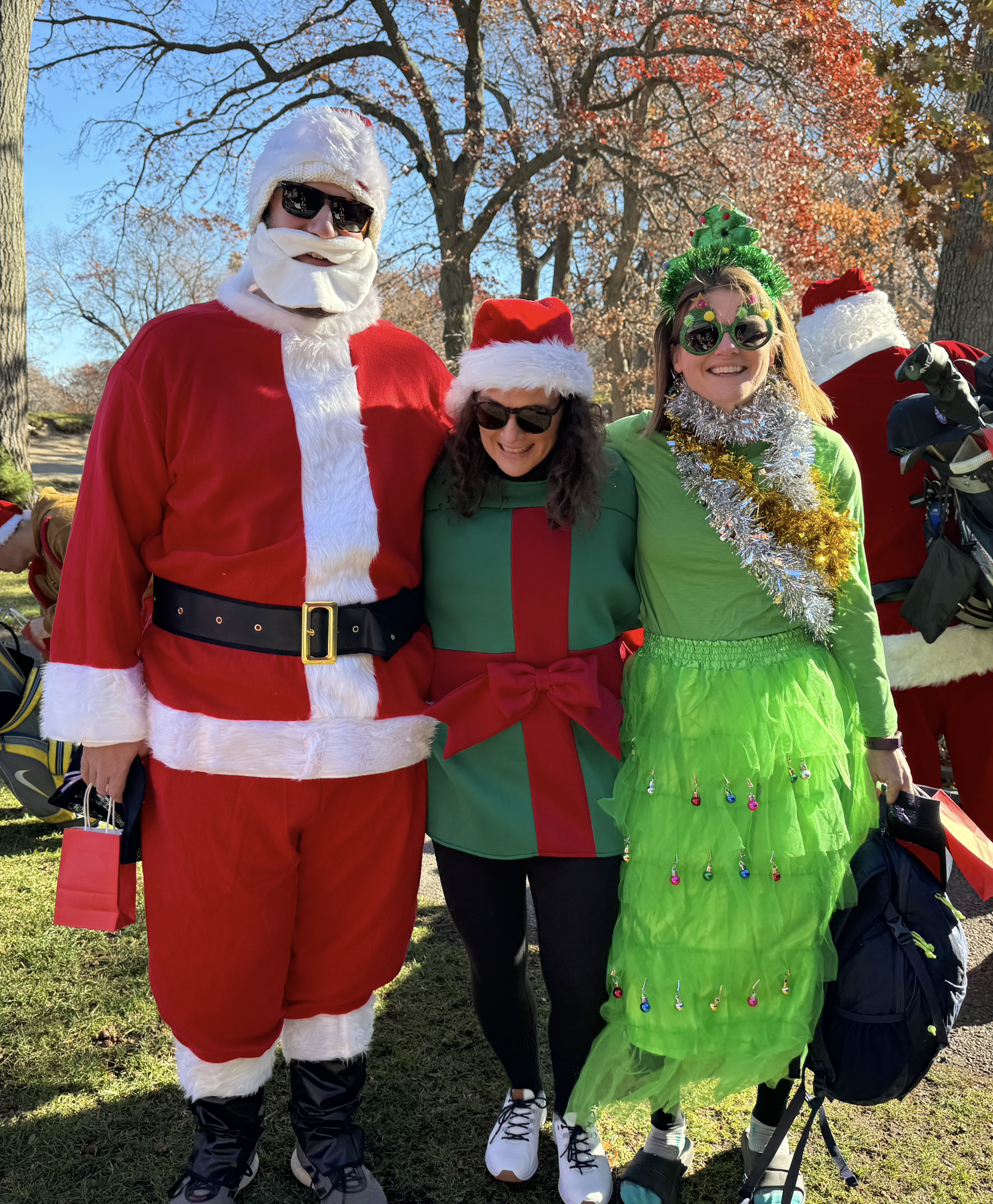 Group of people dressed as Santa Claus, an elf, and a Christmas tree posing outdoors in autumn.