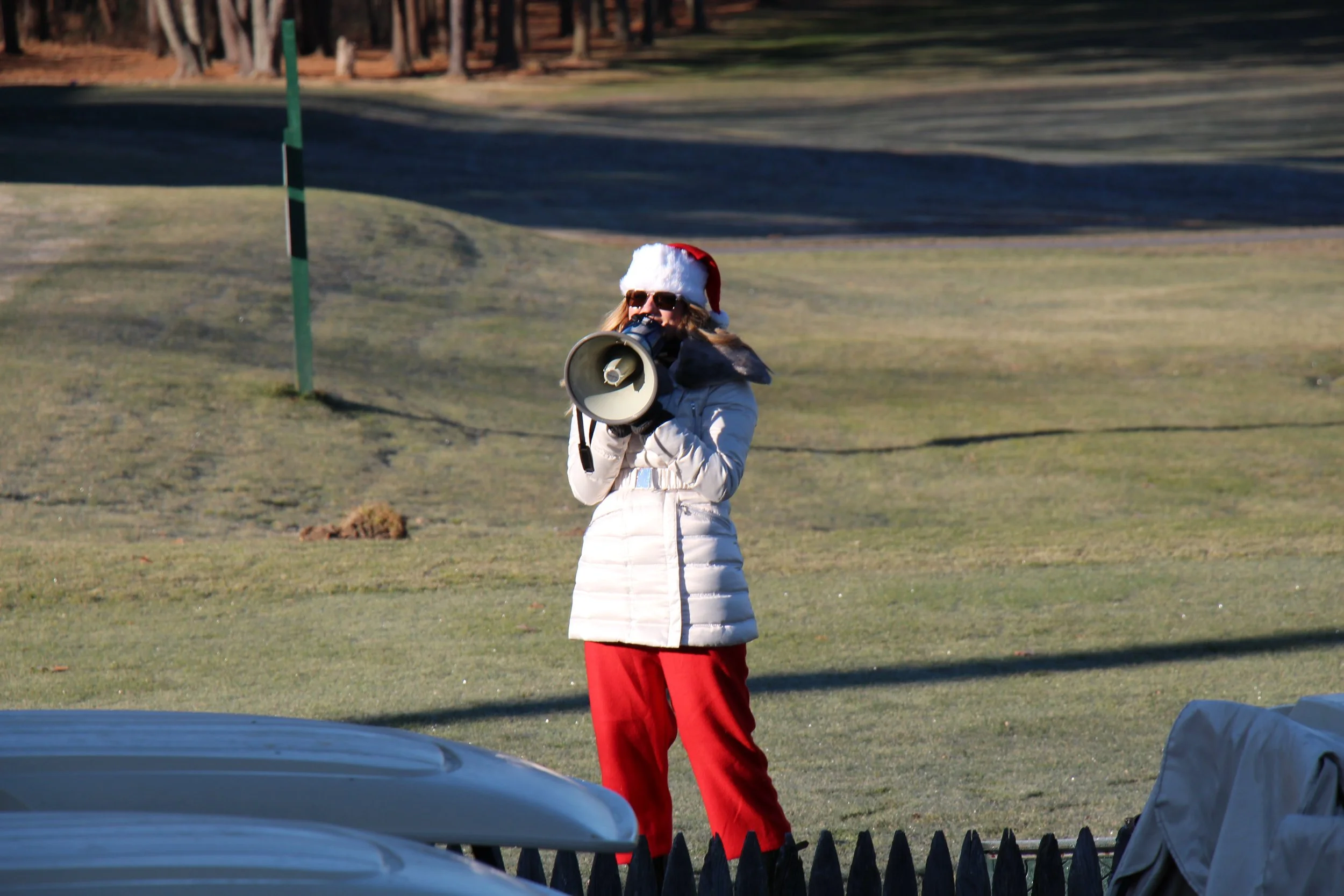 Person wearing a Santa hat and sunglasses speaking through a megaphone outdoors
