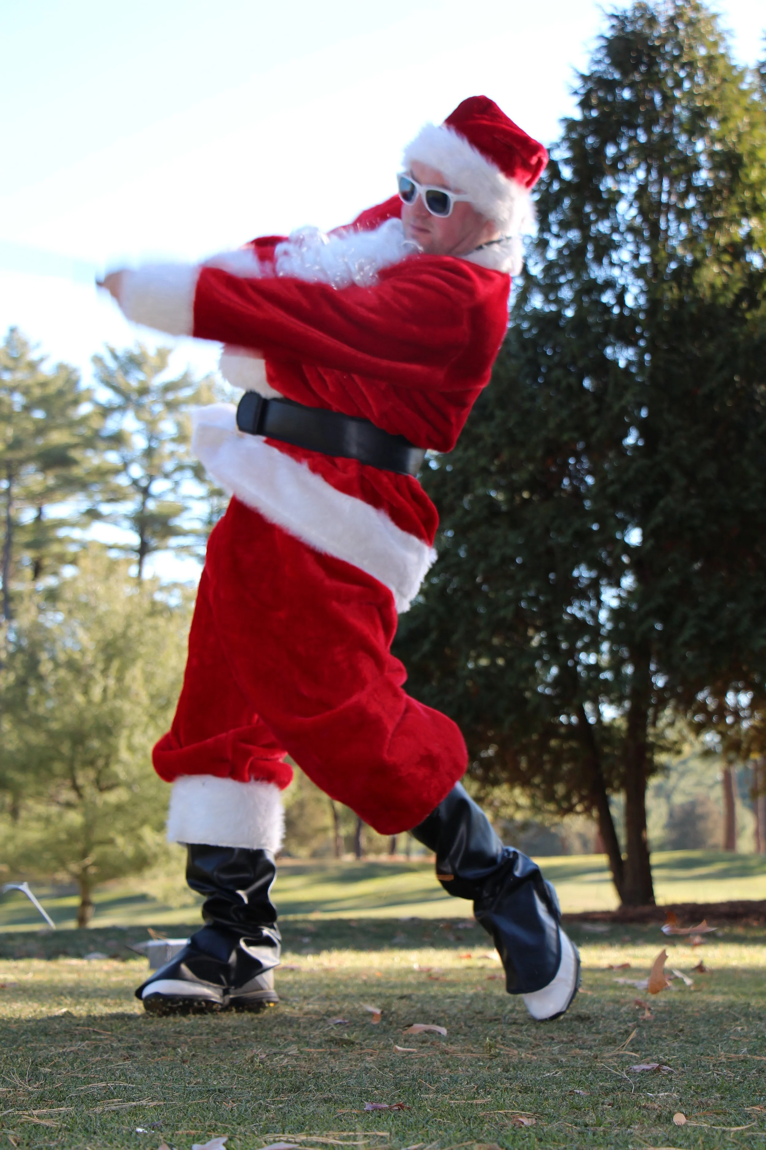Person dressed as Santa Claus wearing sunglasses and dancing outdoors in a park