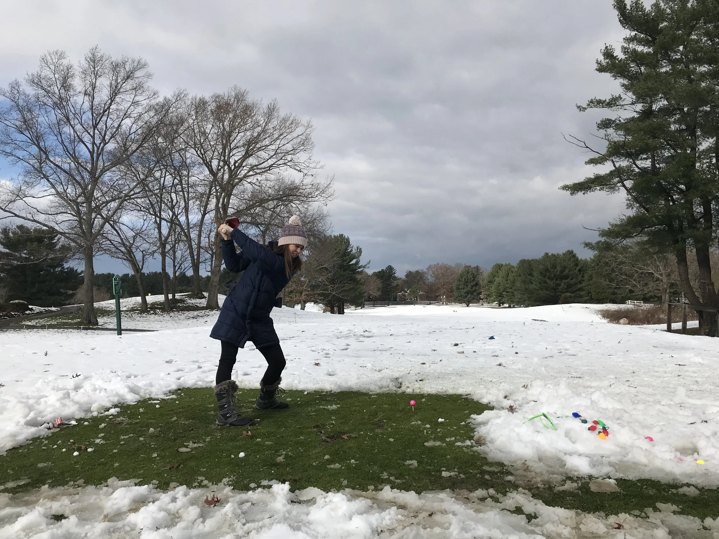 Woman in winter clothing swinging a golf club on a snow-covered mini golf course