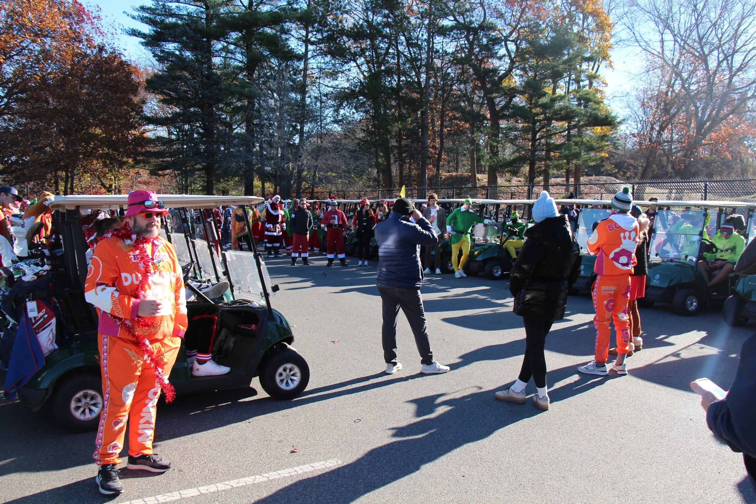 Crowd in festive costumes gathered around golf carts at an outdoor holiday event in a wooded park