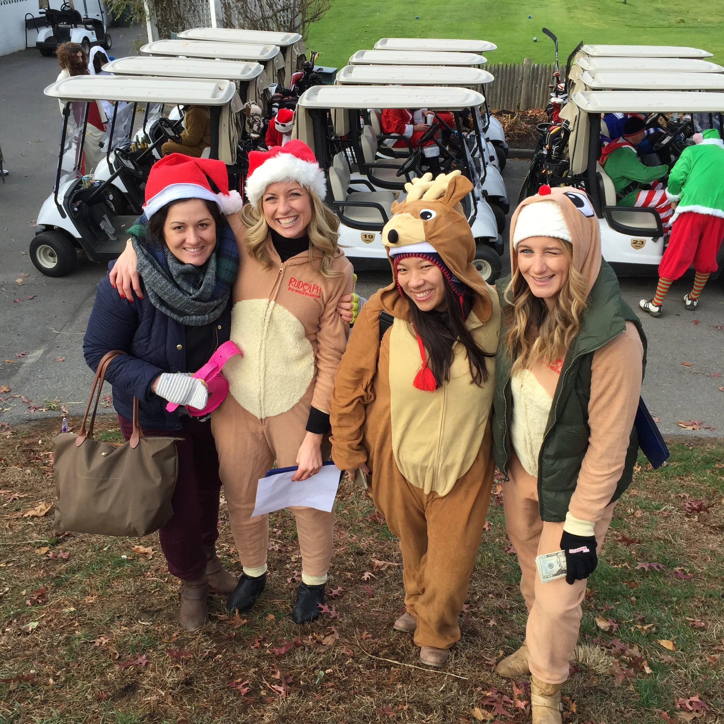 Group of people in Santa, reindeer, and elf costumes posing beside decorated golf carts.