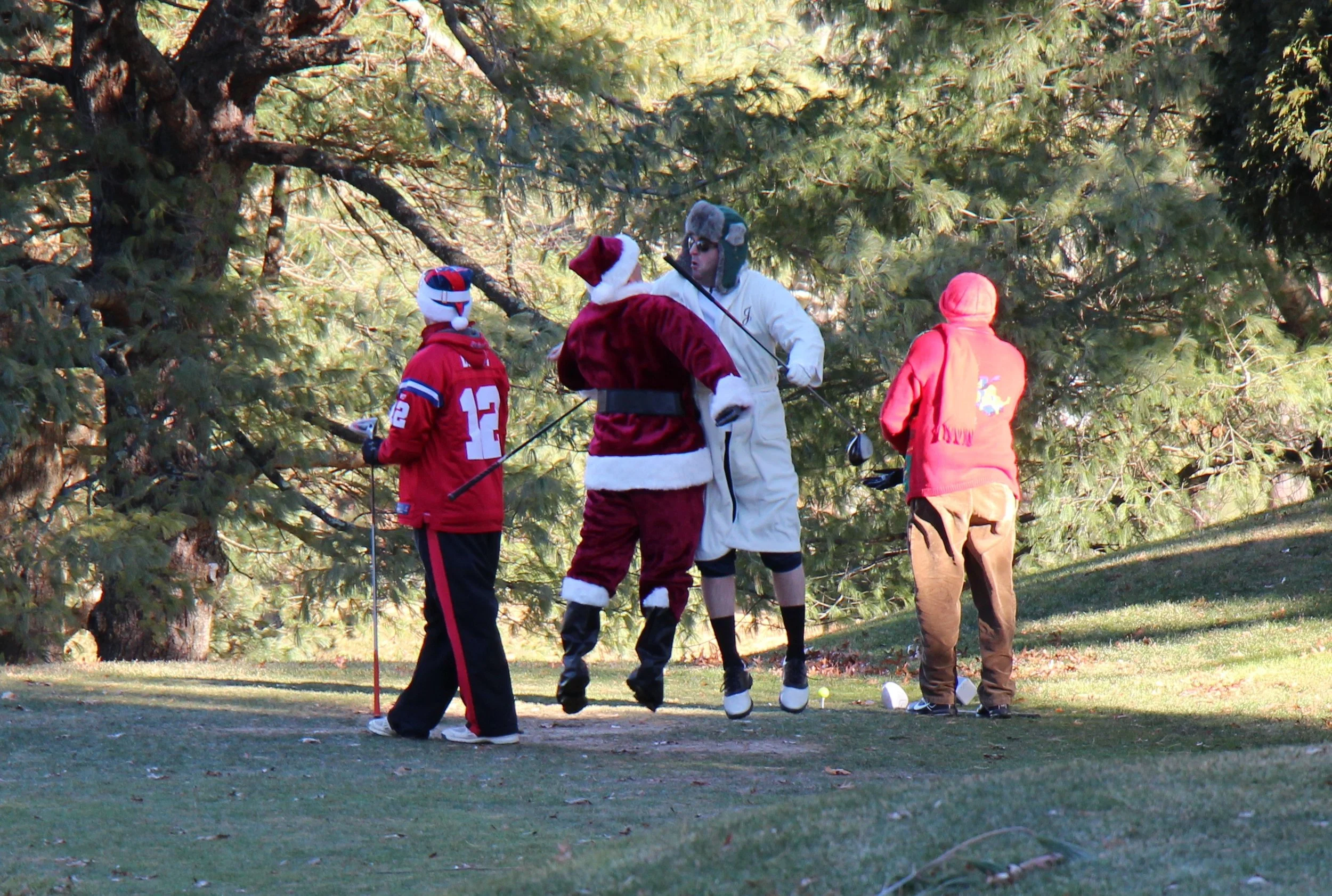 People in Santa Claus and holiday costumes playing golf outdoors among pine trees