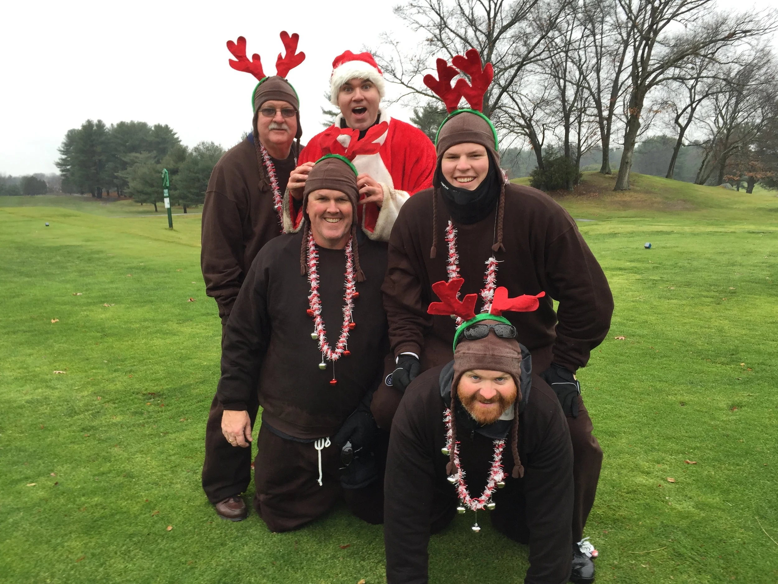 Group of people dressed in Christmas-themed reindeer costumes posing on a golf course