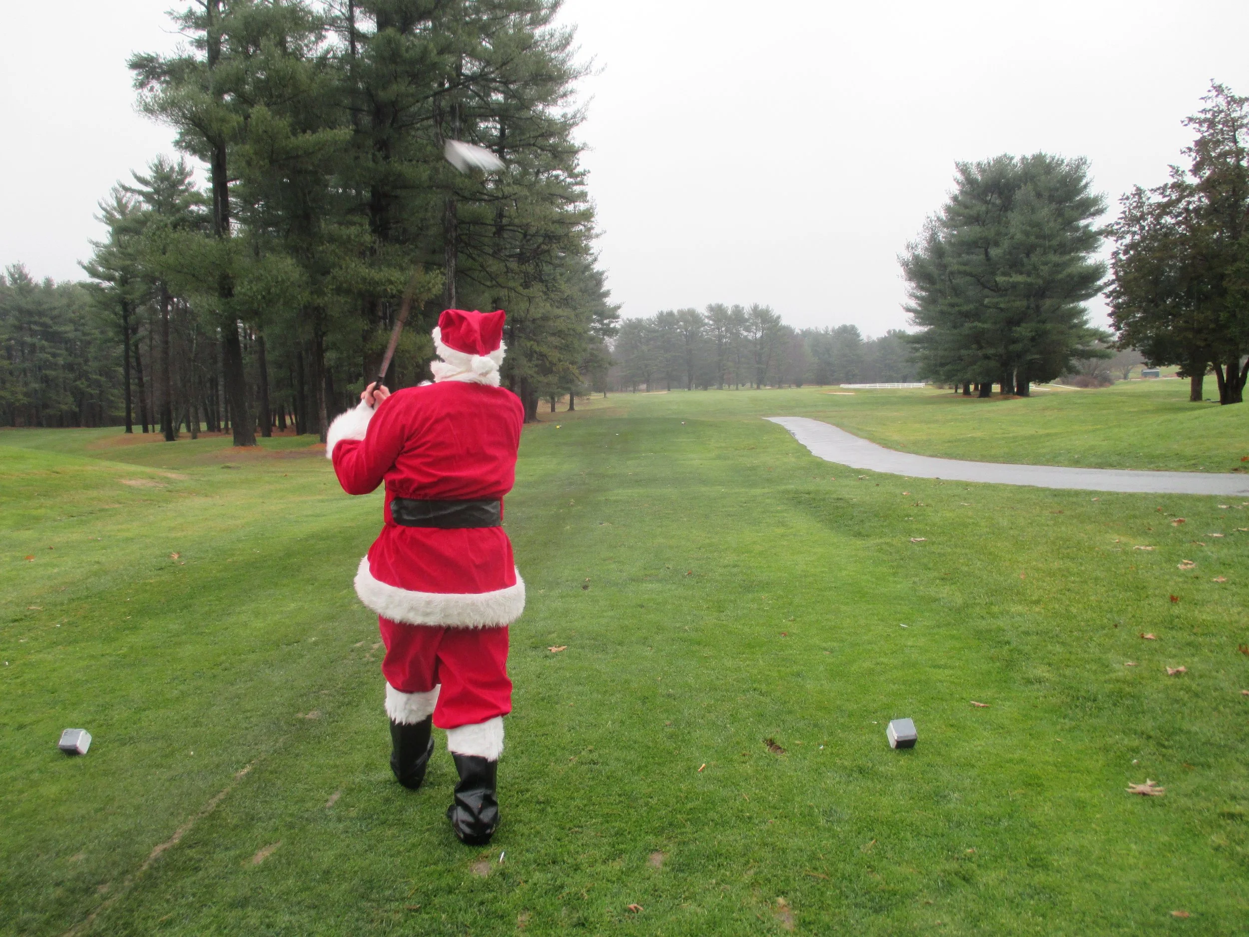Person dressed as Santa Claus playing golf on a misty, tree-lined golf course.