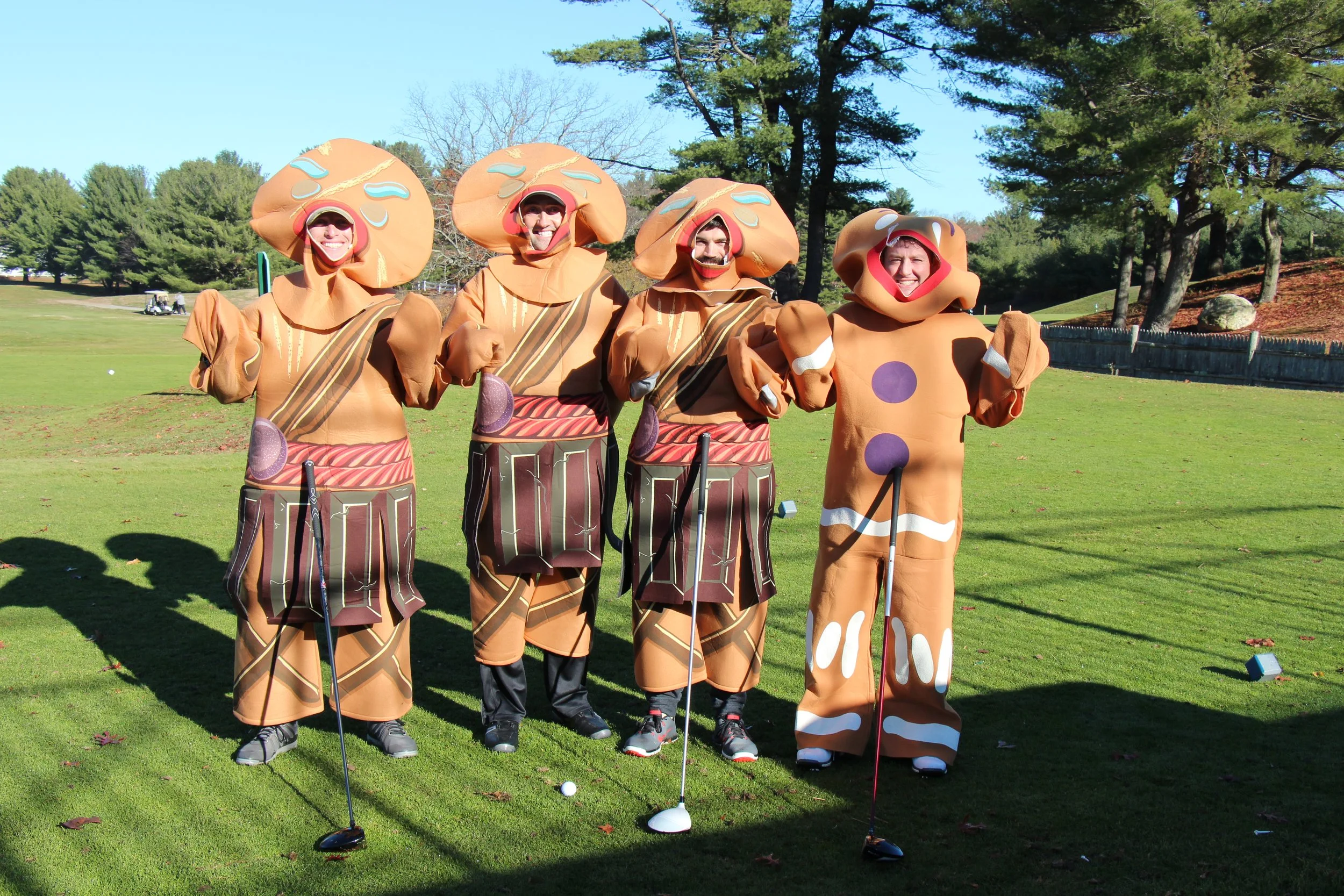 Four people in orange fantasy costumes posing with golf clubs on a sunny golf course