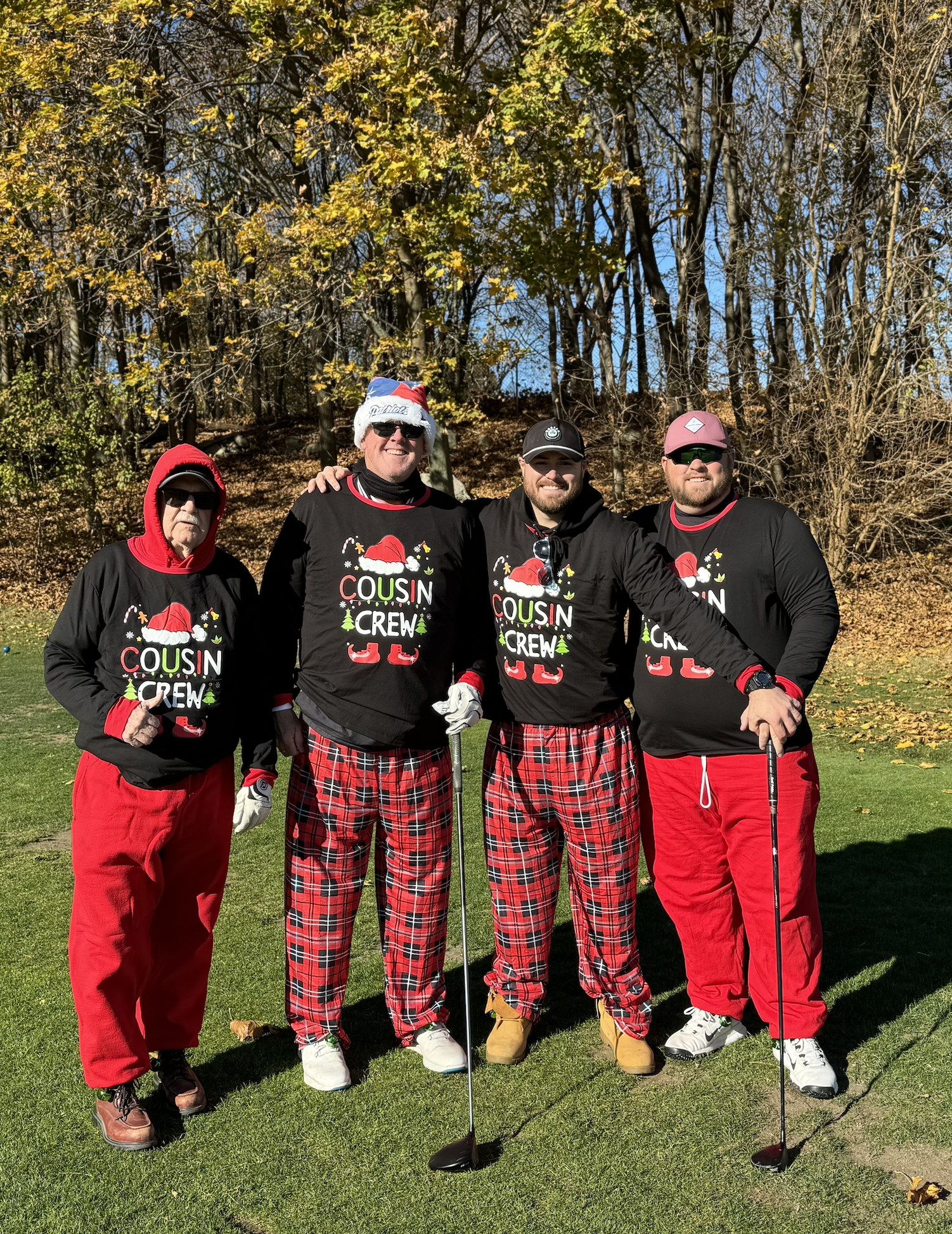 Four men in matching Cousin Crew Christmas shirts and red pants pose with golf clubs on a sunny golf course.