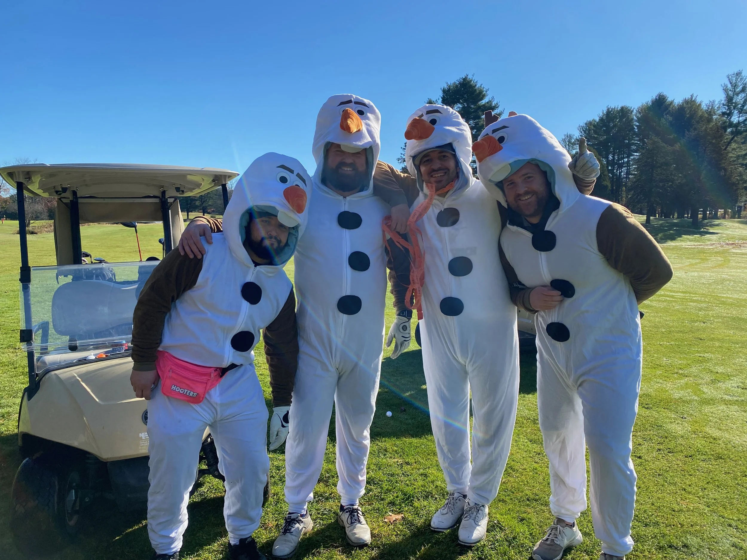 Five people wearing Olaf snowman costumes pose beside a golf cart on a sunny golf course.