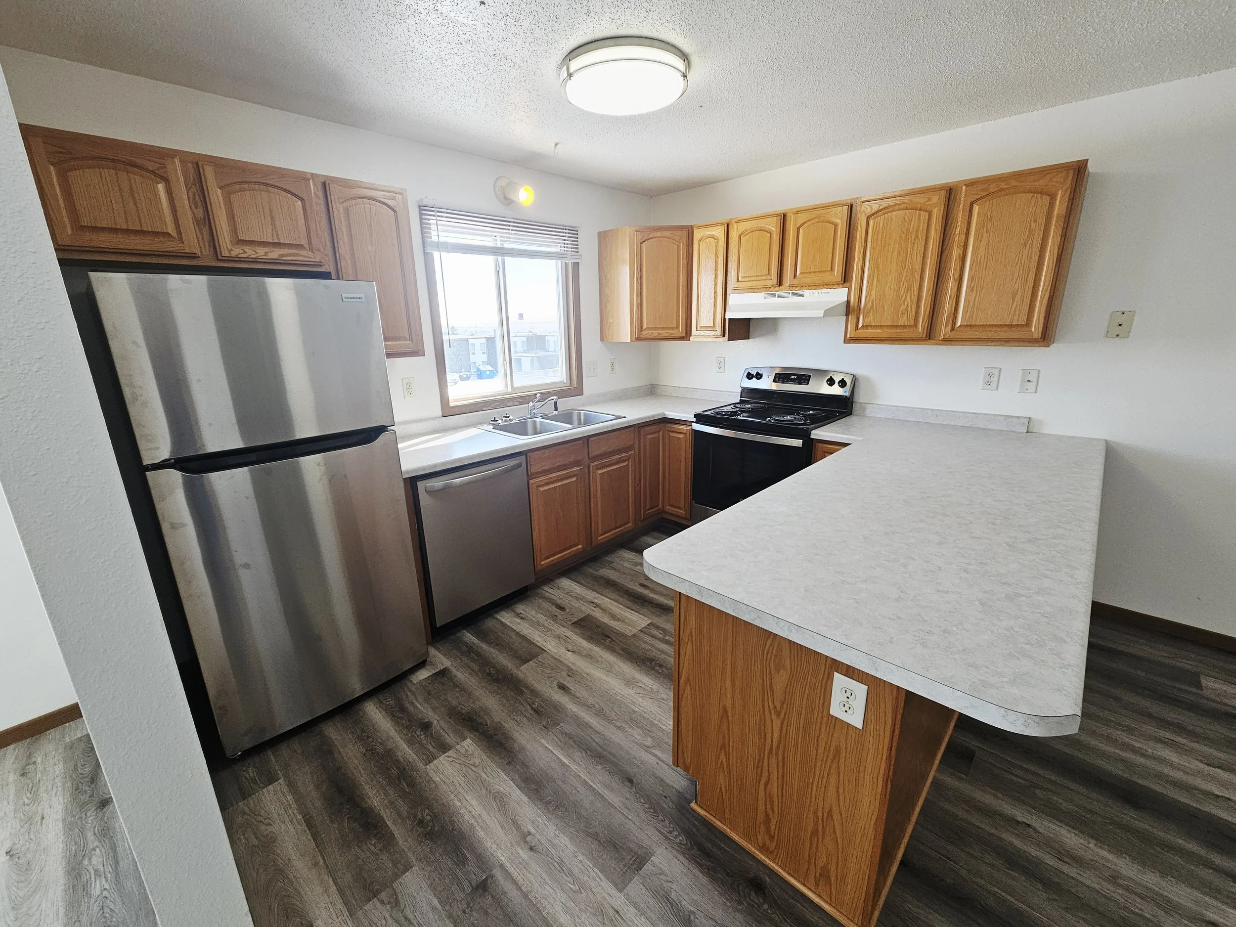 Kitchen with wooden cabinets, stainless steel refrigerator, black stove, white range hood, double sink by window, and a kitchen island.