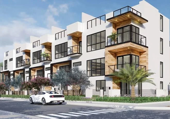 Modern multi-story apartment building with balconies, large windows, and trees lining the sidewalk.