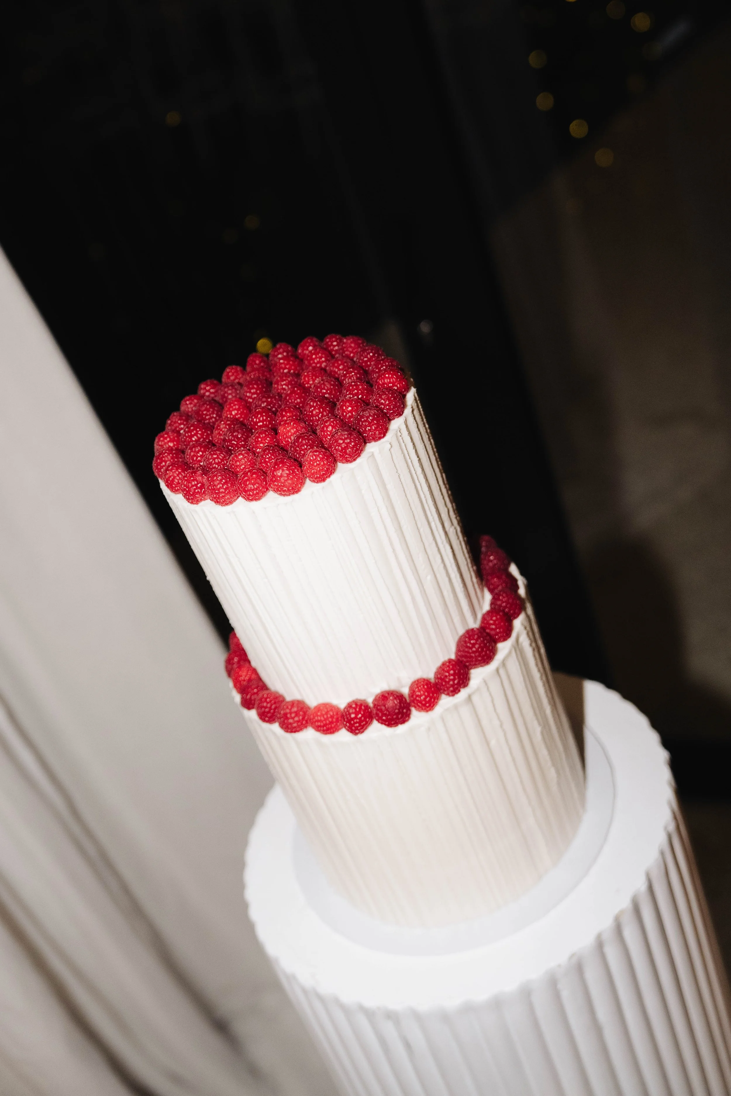 A two-tier wedding cake decorated with white buttercream and raspberries