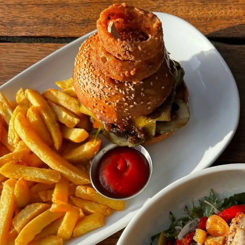 Burger with onion rings on top, served with French fries and ketchup, with a side salad partially visible.